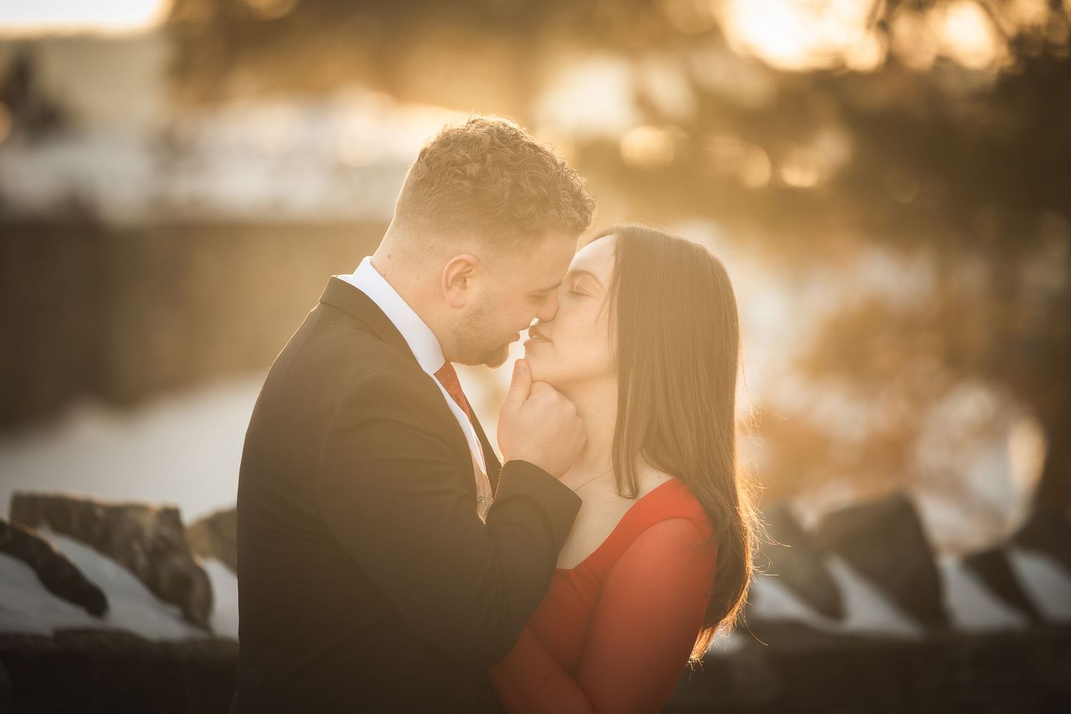 A romantic couple shares an intimate moment at sunset, with the woman wearing red and the man in a dark suit.
