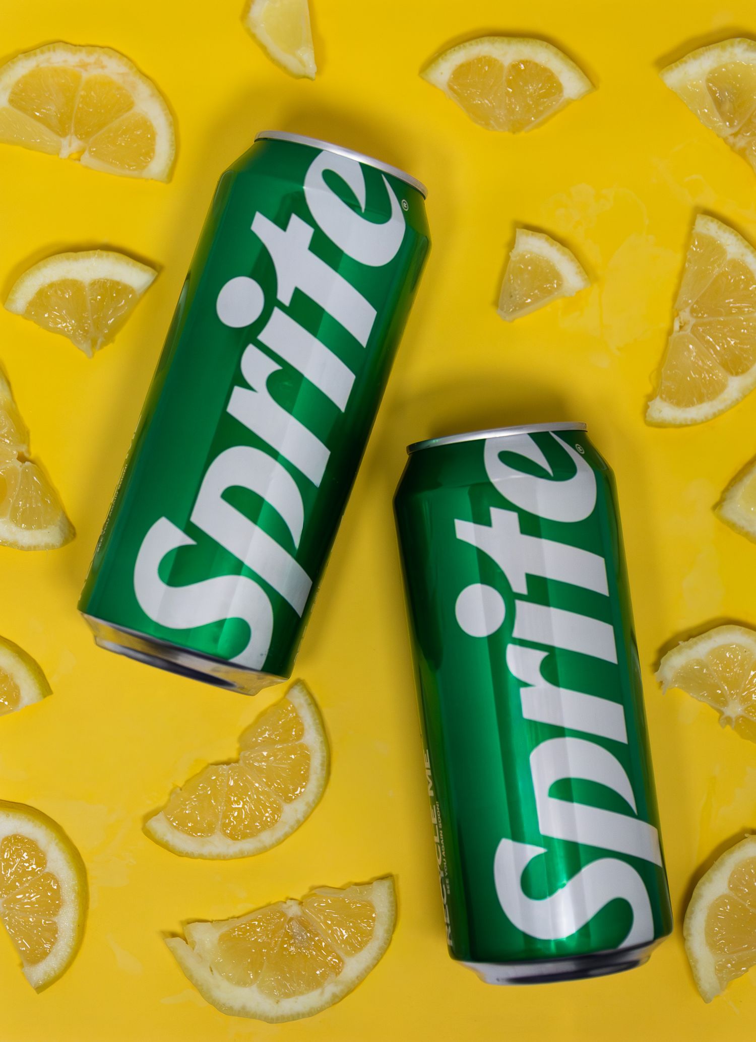 Two green Sprite cans surrounded by fresh lemon slices on a bright yellow background.