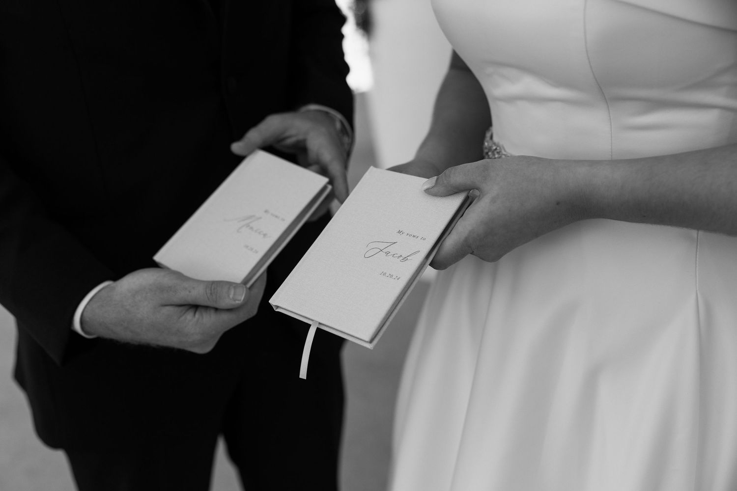 Black and white photo of bride and groom holding personalized wedding vow booklets at ceremony.