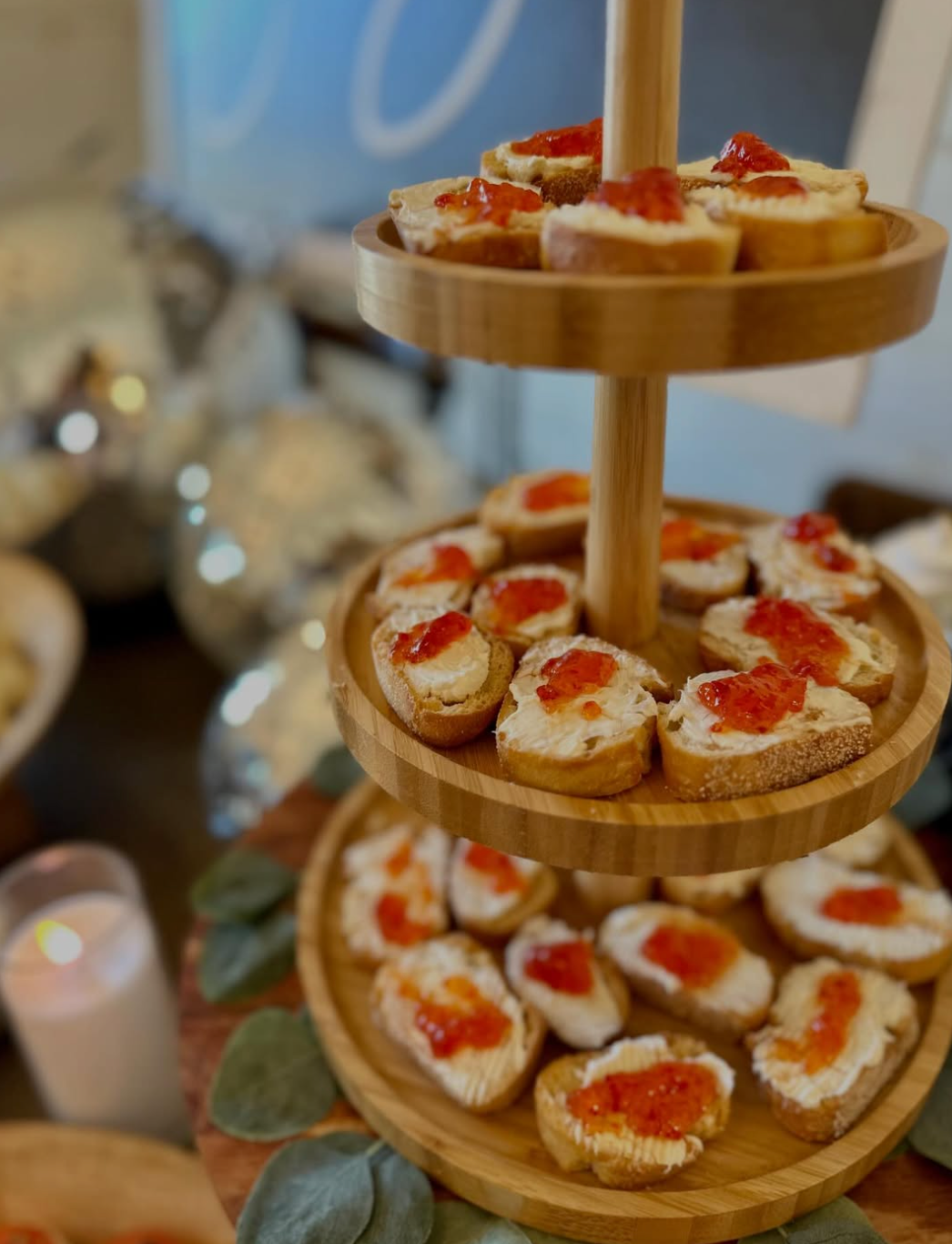 Three-tier wooden serving stand displaying bruschetta topped with cream cheese and red pepper jelly at an elegant event.