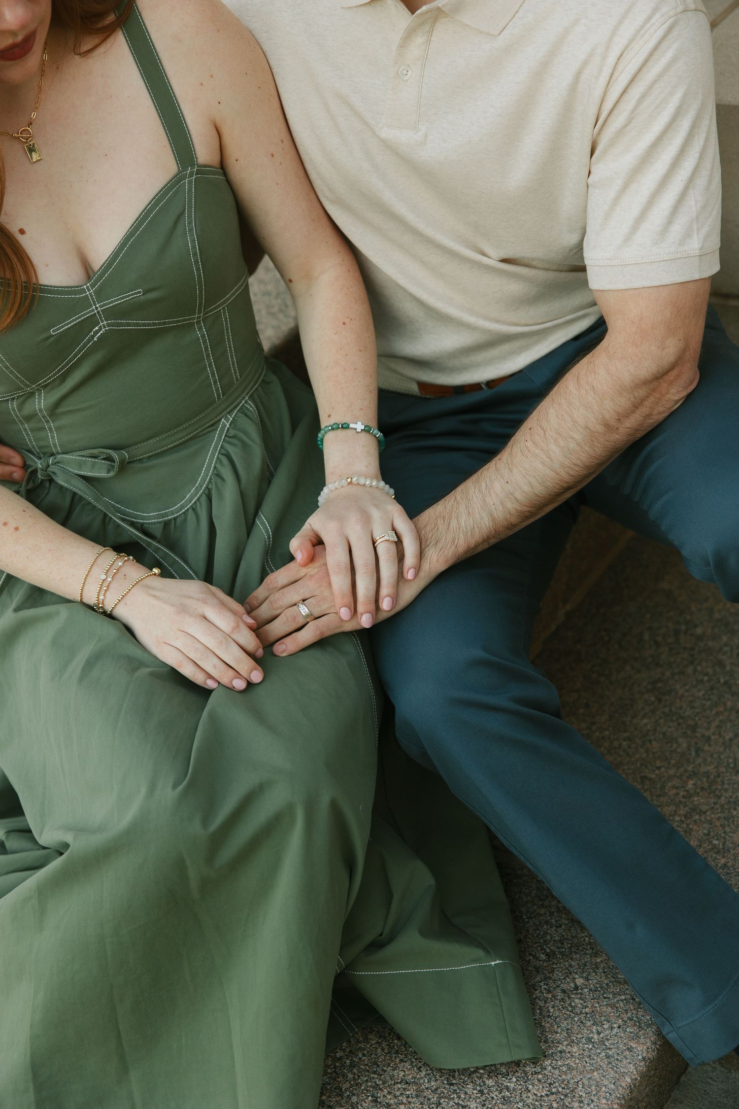 A couple in an engagement session holds hands, she wears a green dress and he wears blue pants.