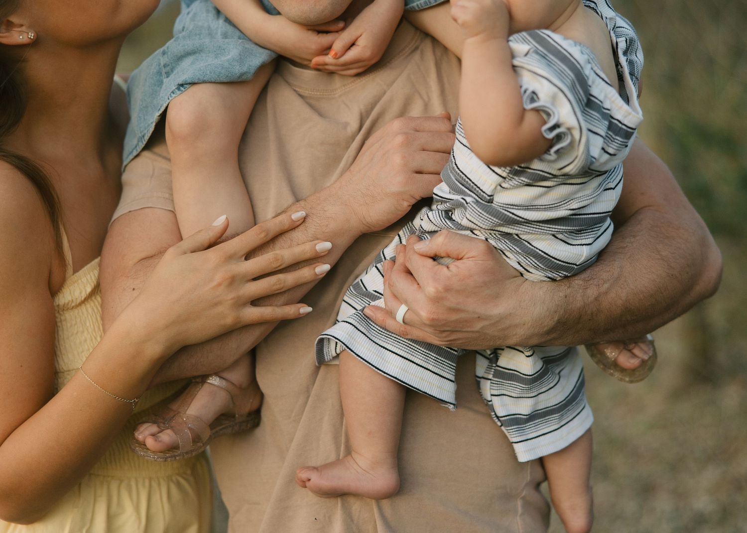 Two parents cradle two young babies in their arms in a warm outdoor family portrait.