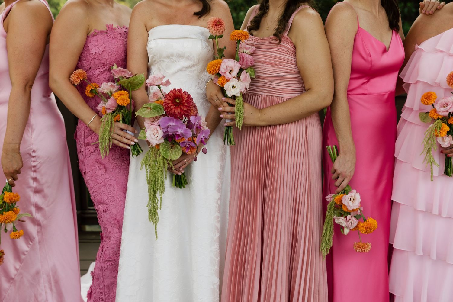 Bride in white gown with bridesmaids in pink dresses holding colorful floral bouquets at a wedding.