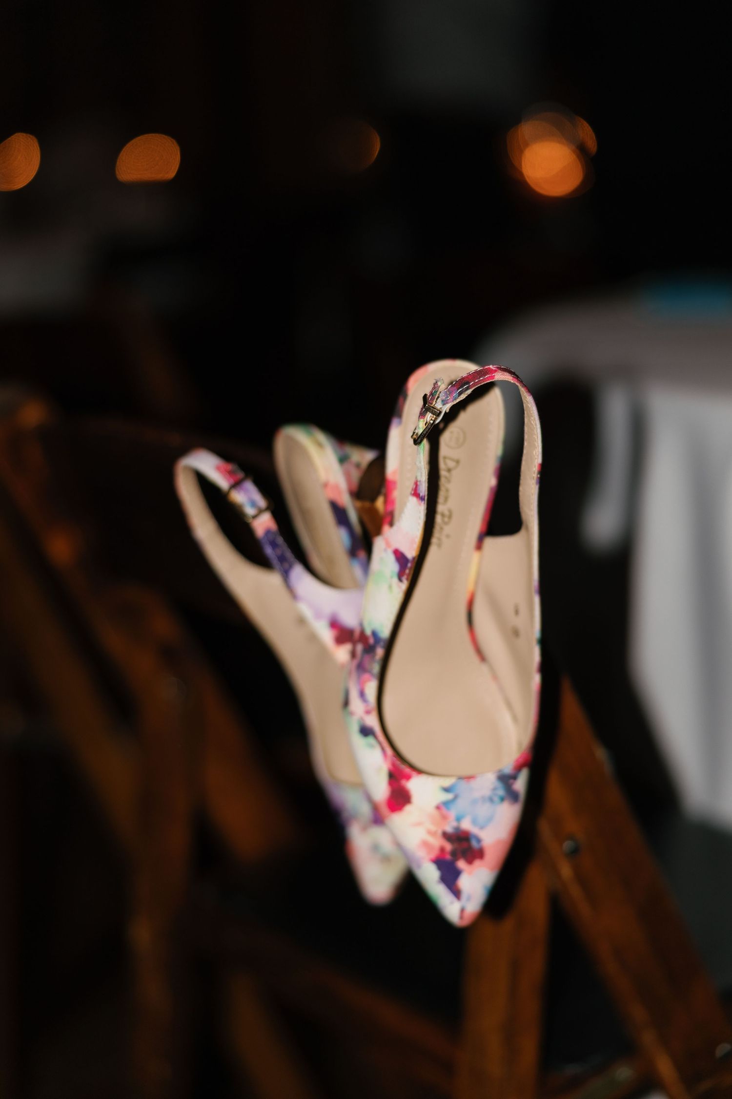 Floral slingback heels with pink and blue pattern displayed on wooden chair at evening event.
