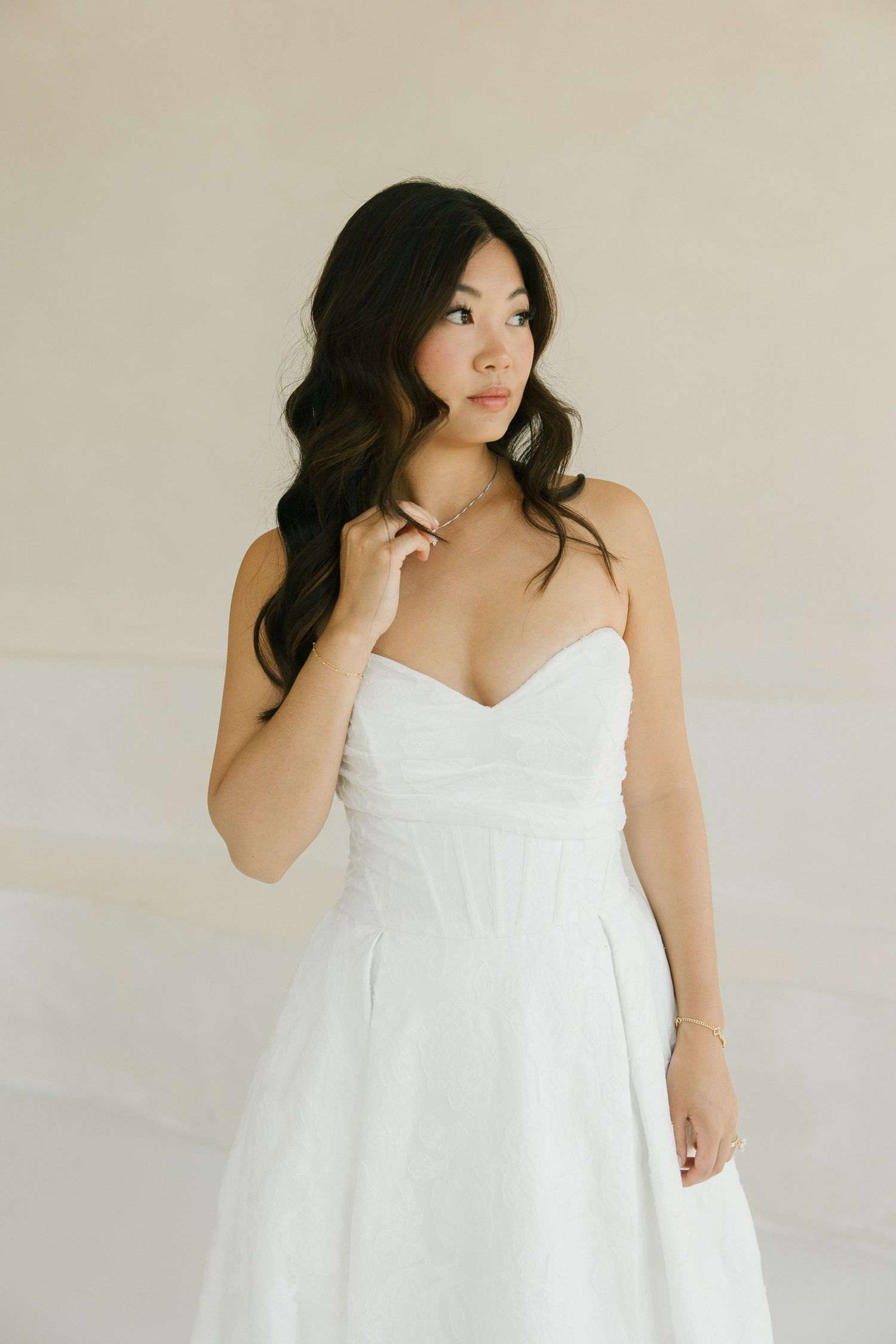 Asian bride in strapless sweetheart white gown with wavy dark hair and delicate earrings.
