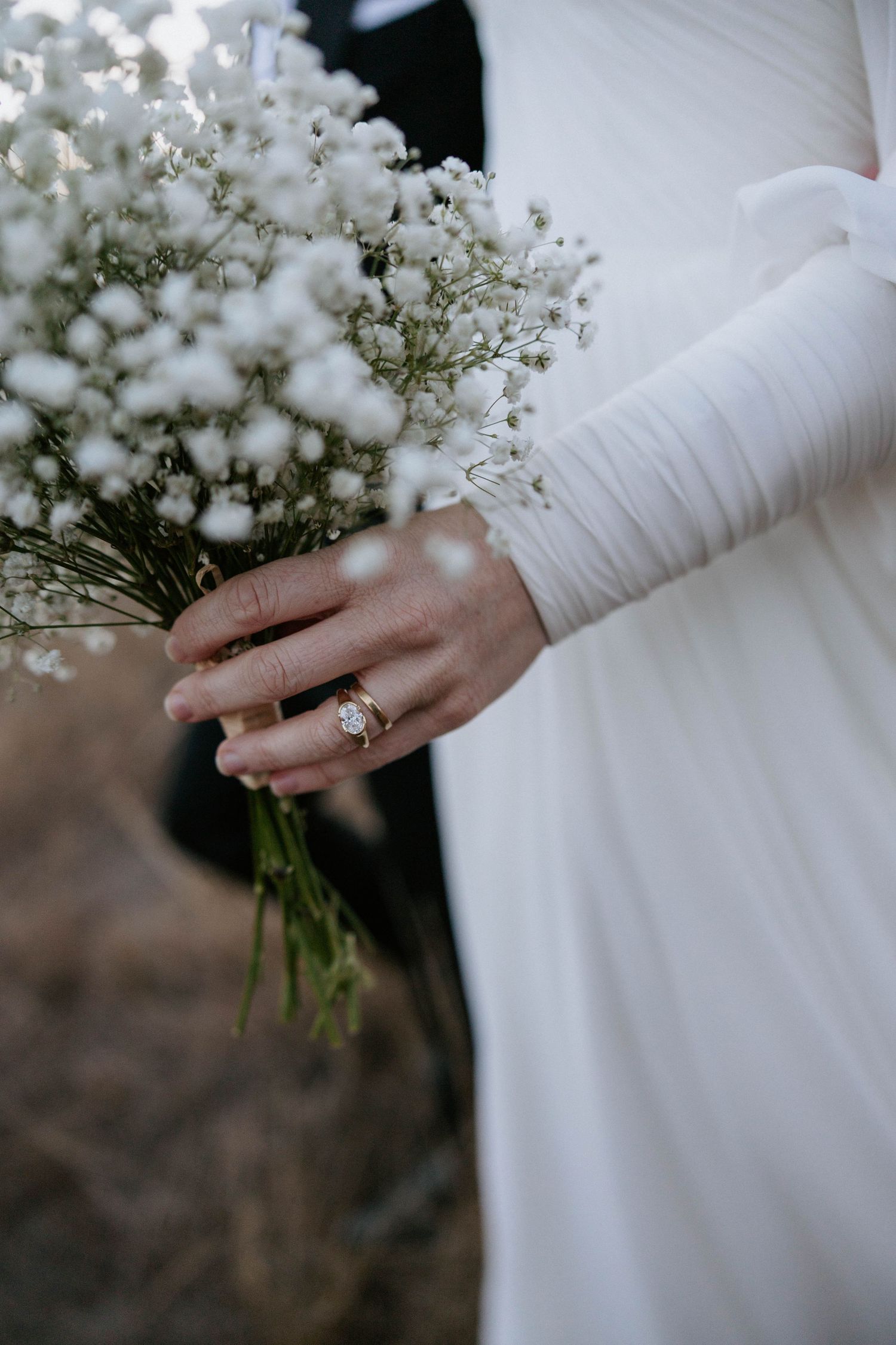 Bride in white dress holding baby's breath bouquet with gold diamond engagement ring on her finger.
