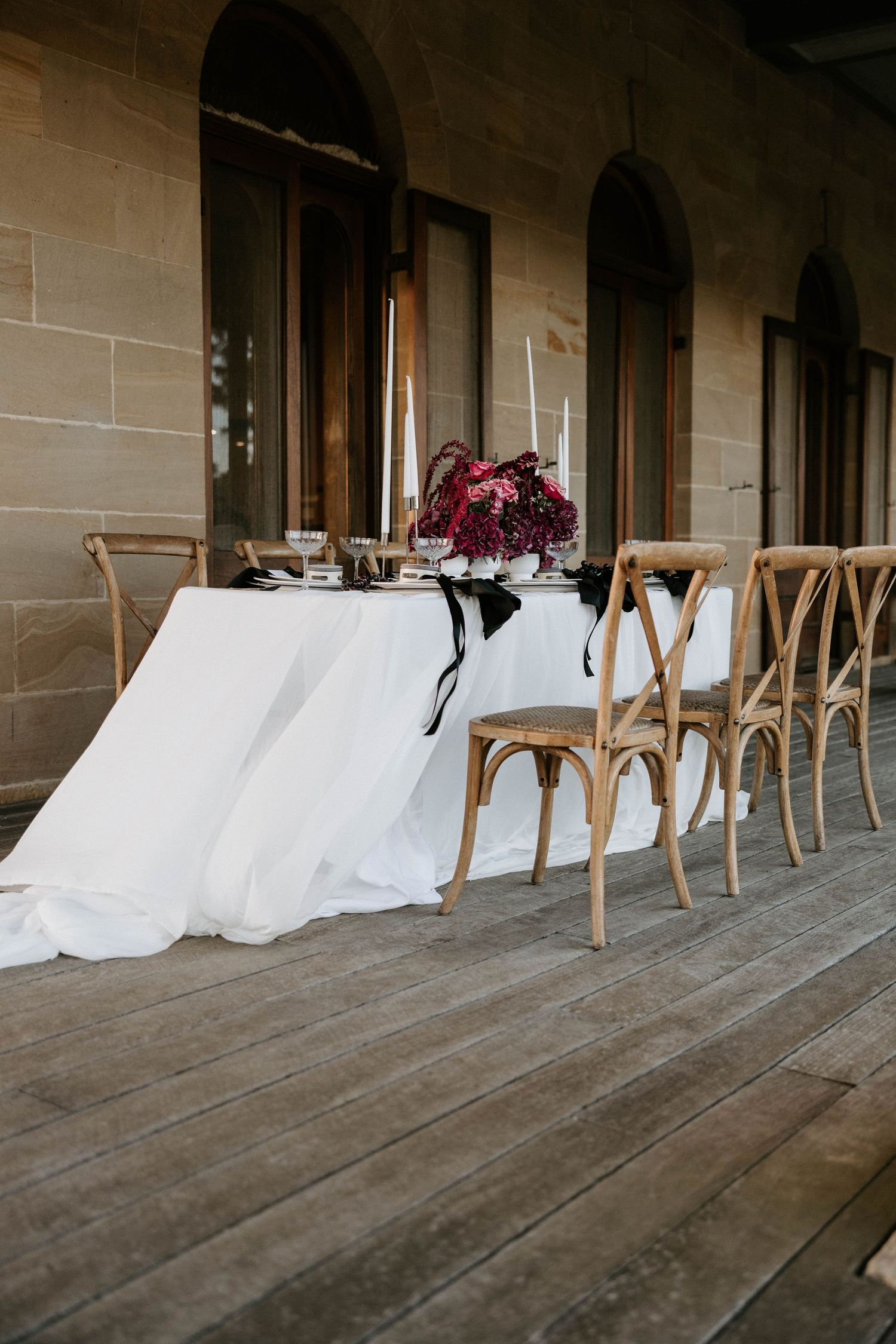 Empty chairs line a covered porch with white fabric draped between them creating an elegant outdoor seating arrangement.