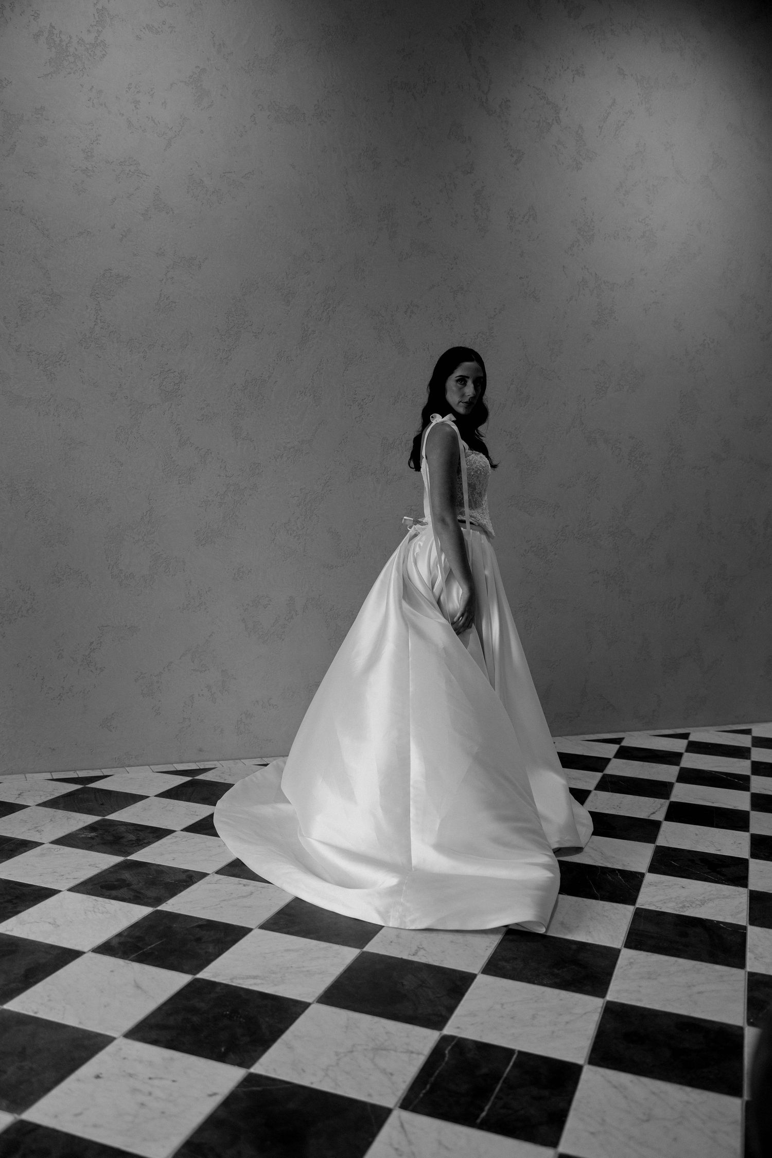 Bride in elegant ball gown poses on checkered floor in black and white wedding portrait photo.