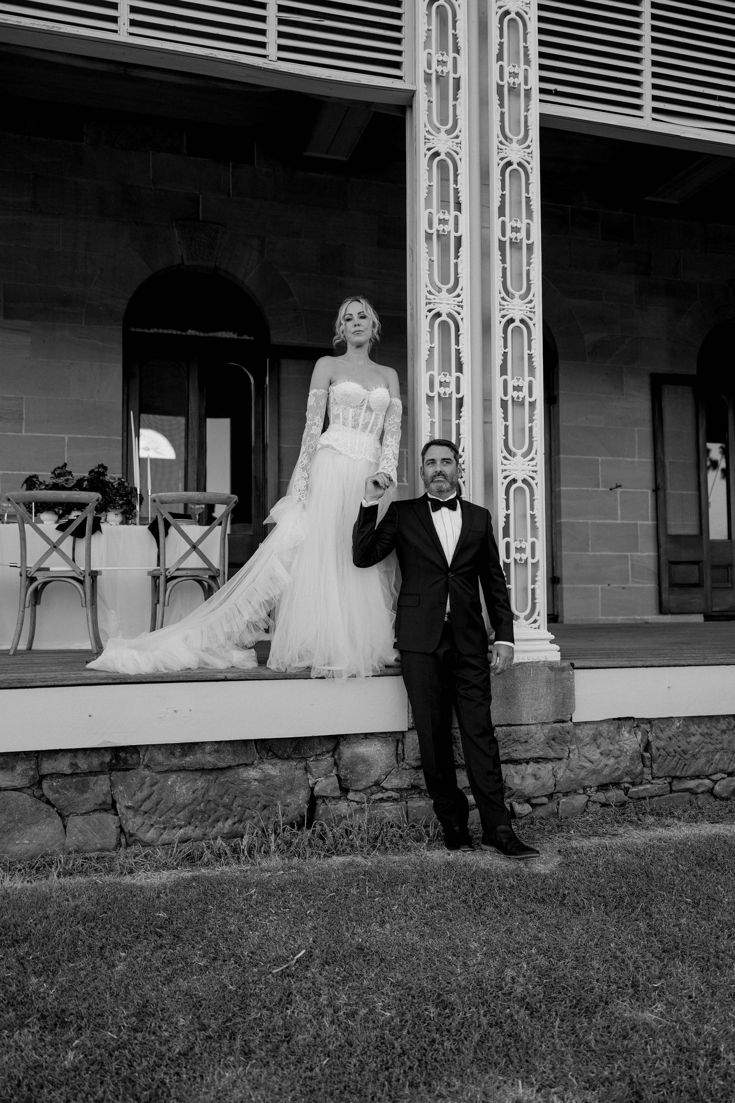 Black and white wedding portrait series showing couple posing along a rustic porch with decorative white columns.