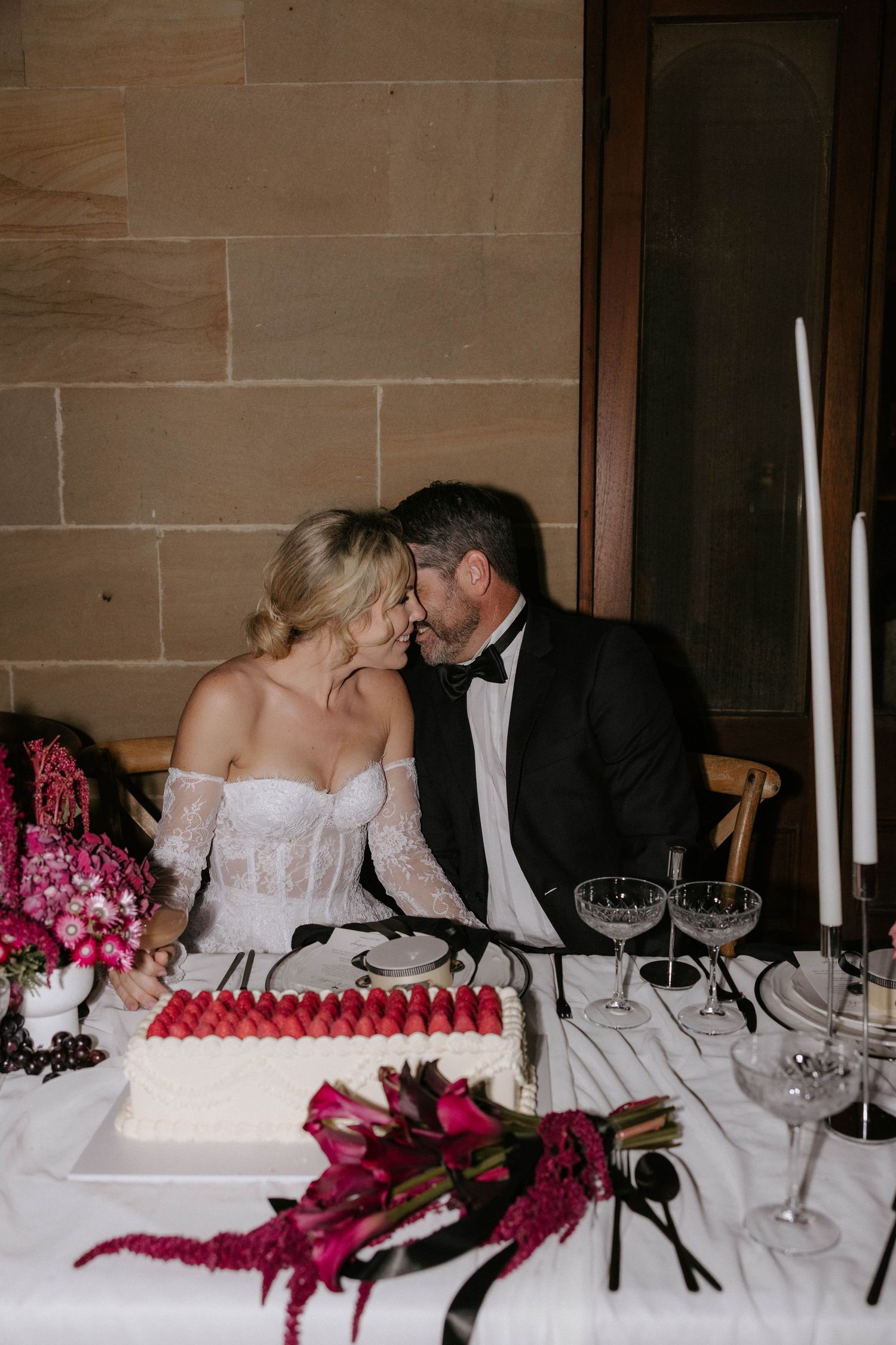 A romantic wedding reception table with white cake, pink flowers, and wine glasses set for an elegant celebration.
