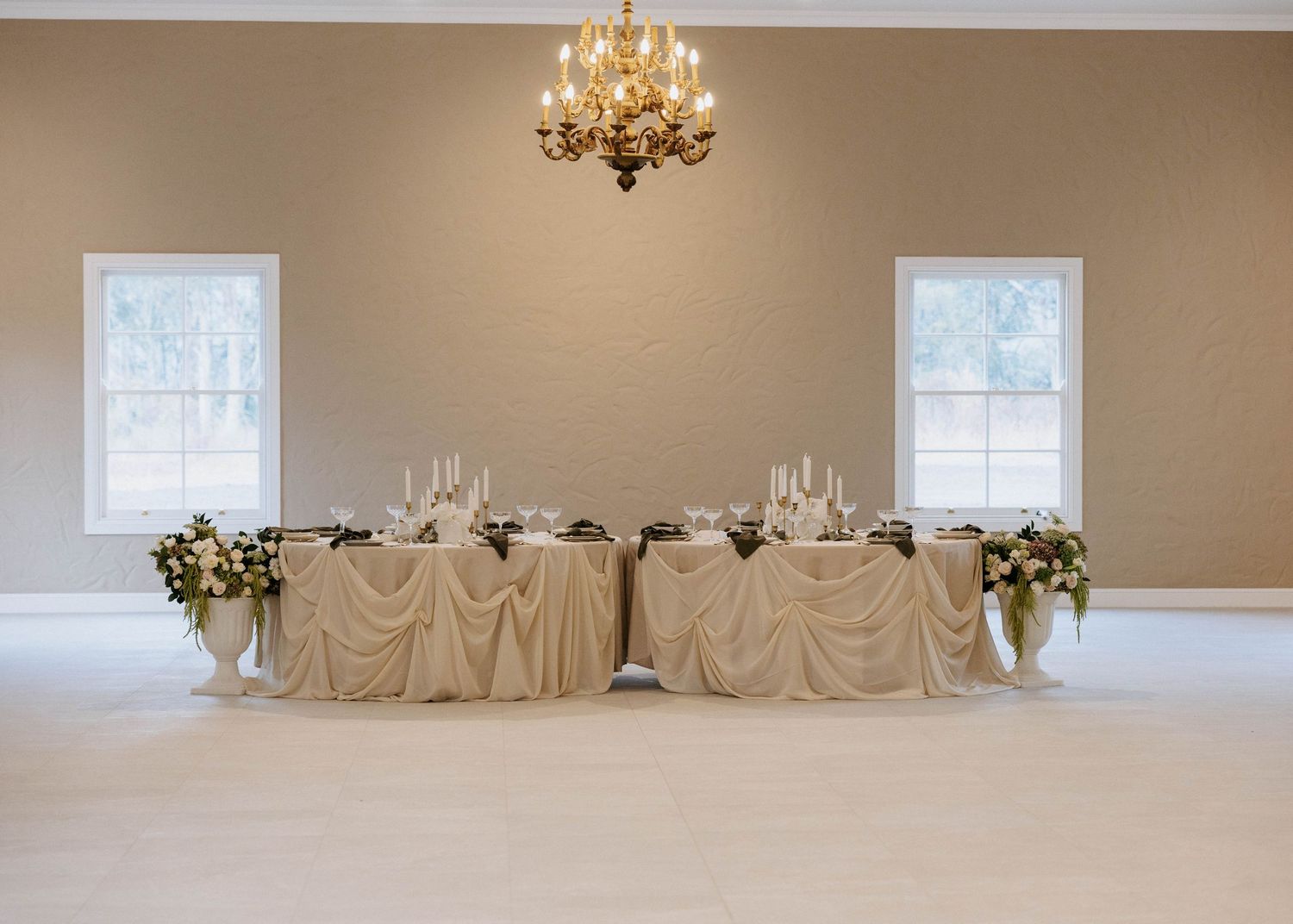 Elegant wedding reception sweetheart table with champagne linens, floral arrangements, and chandelier lighting.