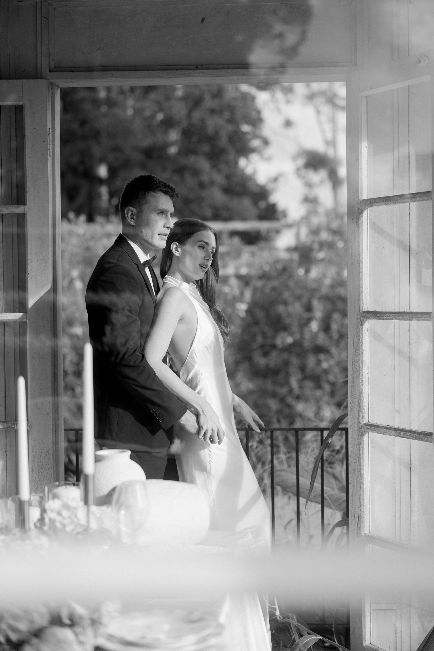 Black and white photo of a bride and groom standing together in an open doorway, gazing outward on their wedding day.