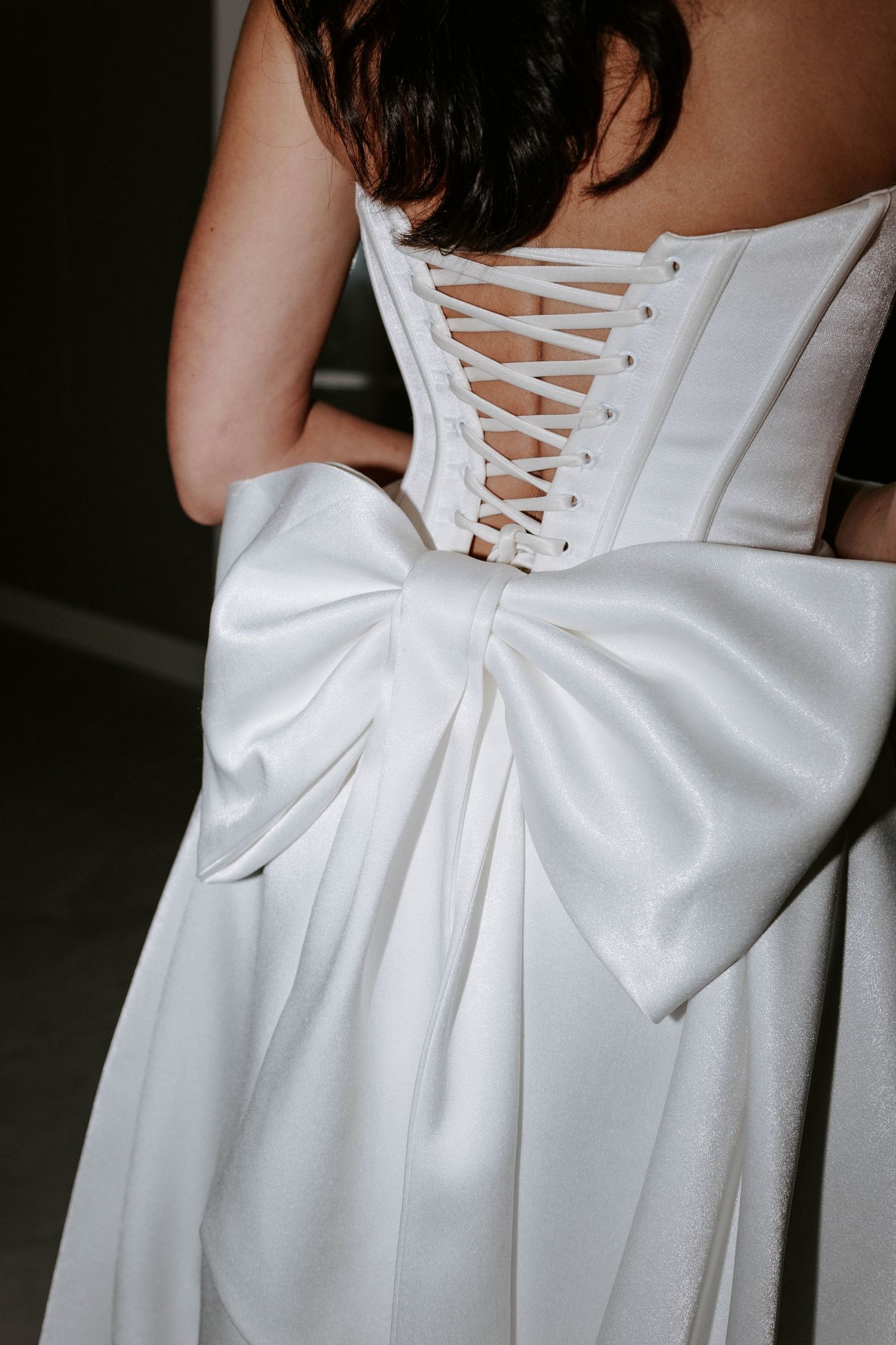 Close-up of bridal gown back featuring corset lacing and large satin bow detail in white.