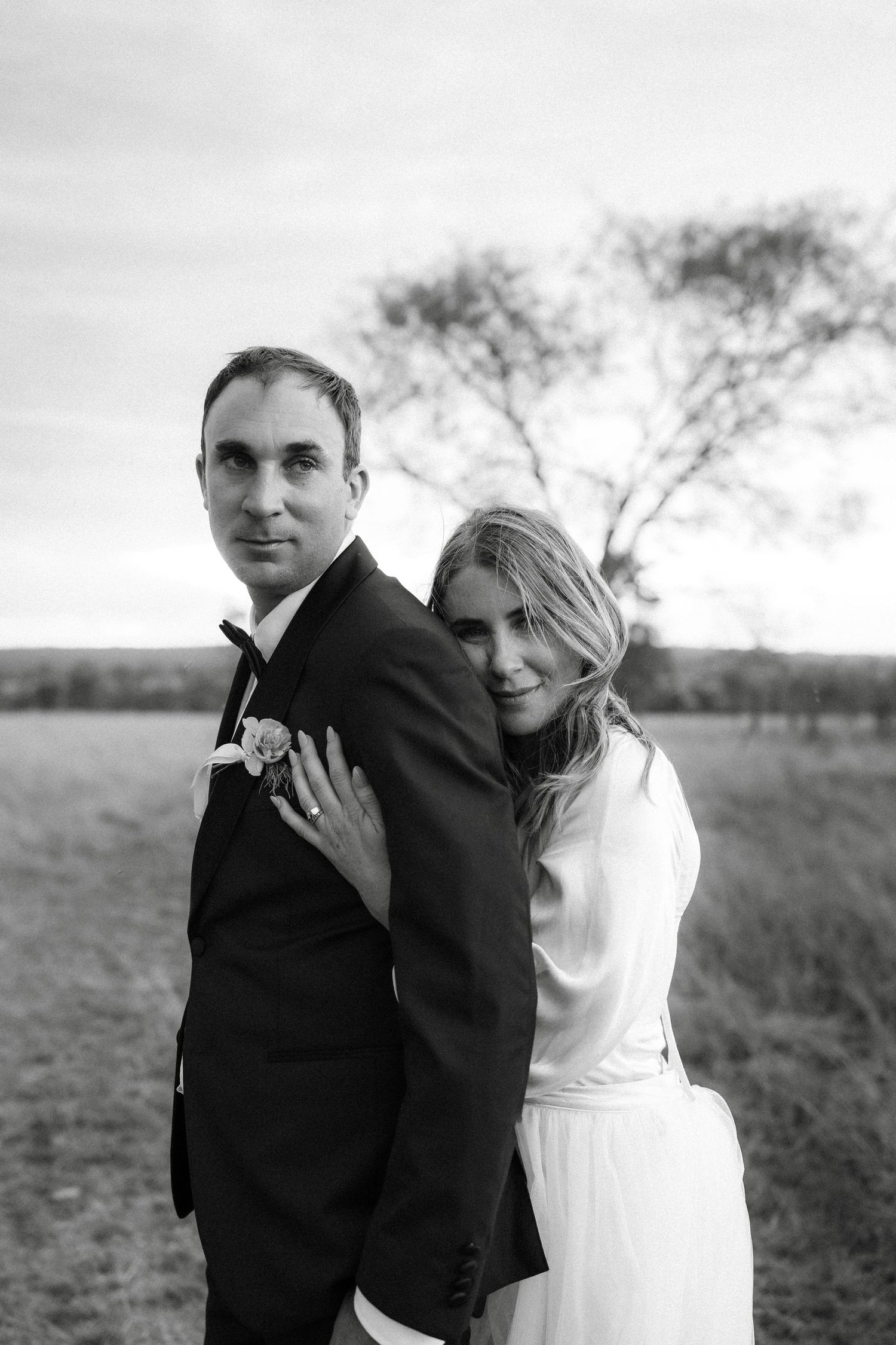A romantic black and white photo series of a couple embracing in an outdoor field setting.