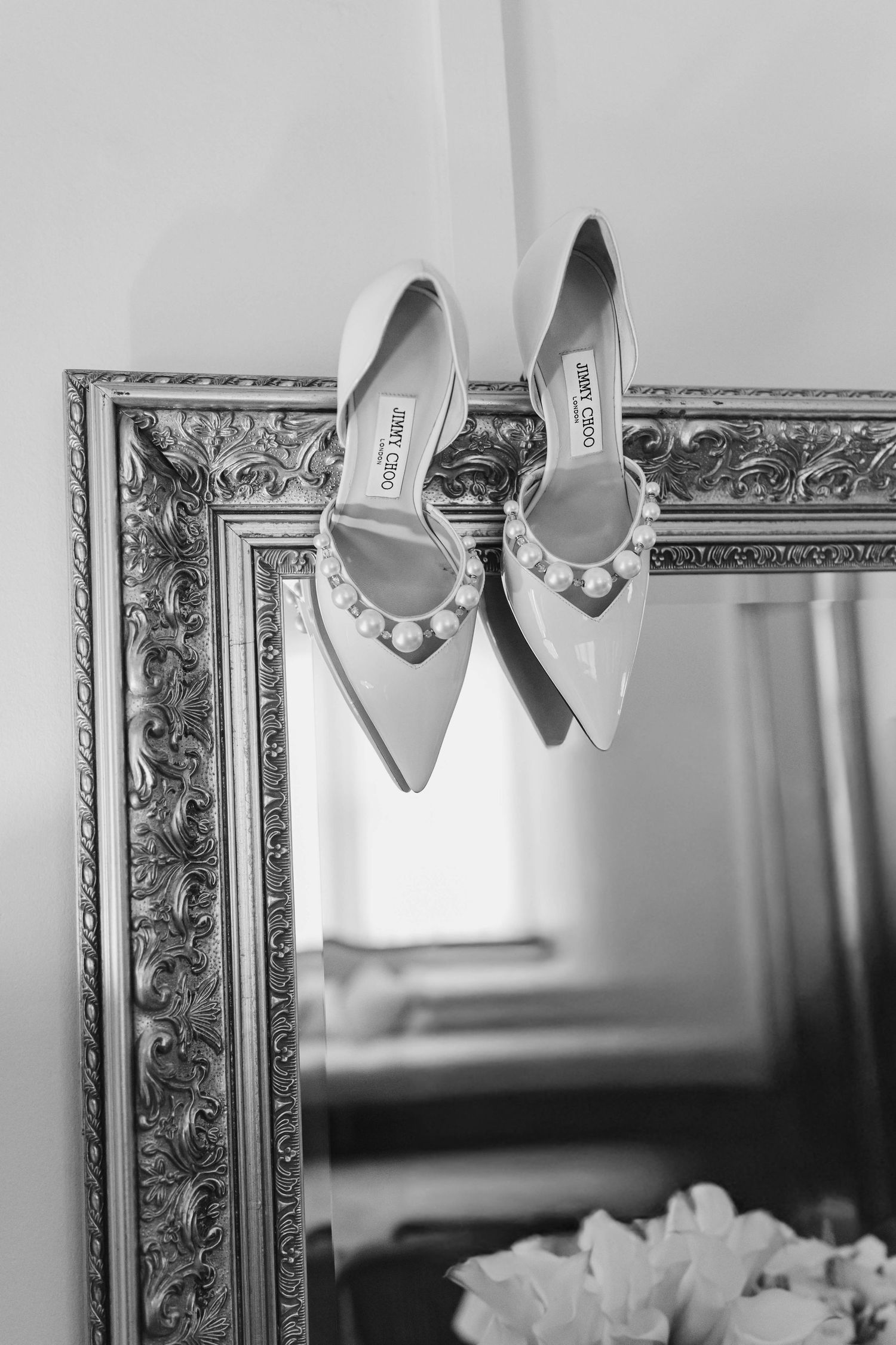 Elegant silver pointed-toe bridal shoes displayed against an ornate gilded mirror frame. jimmy Choo wedding shoe details