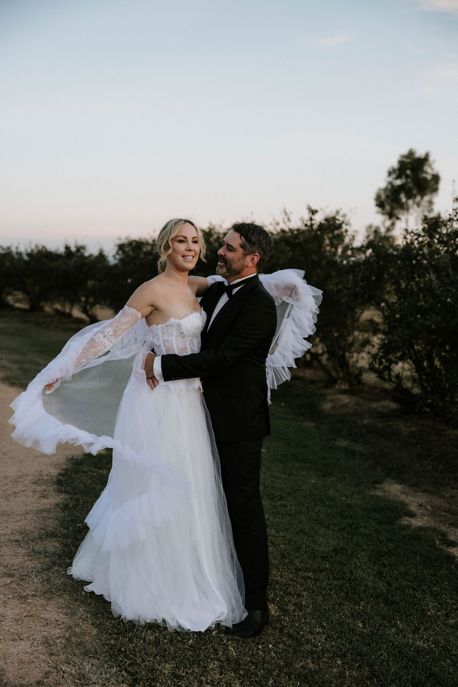 A romantic wedding couple dances together at sunset in a rustic outdoor setting.