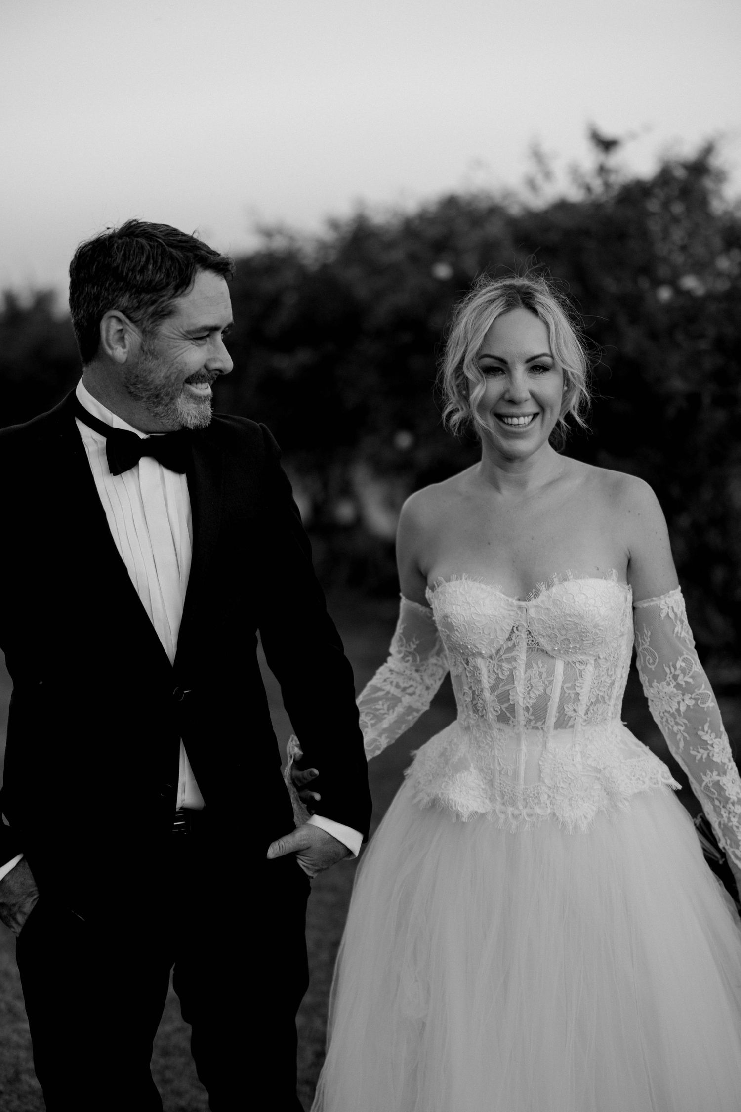 A joyful wedding couple shares candid moments together outdoors in black and white photography.