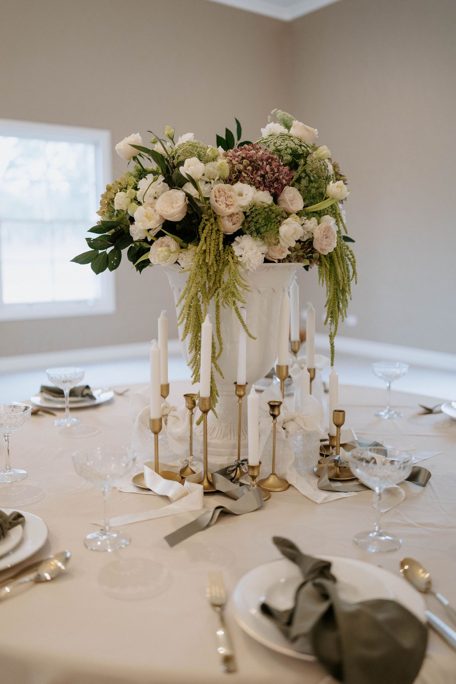 Elegant wedding reception table with tall white floral centerpiece, gold candelabras, and sage green napkins.