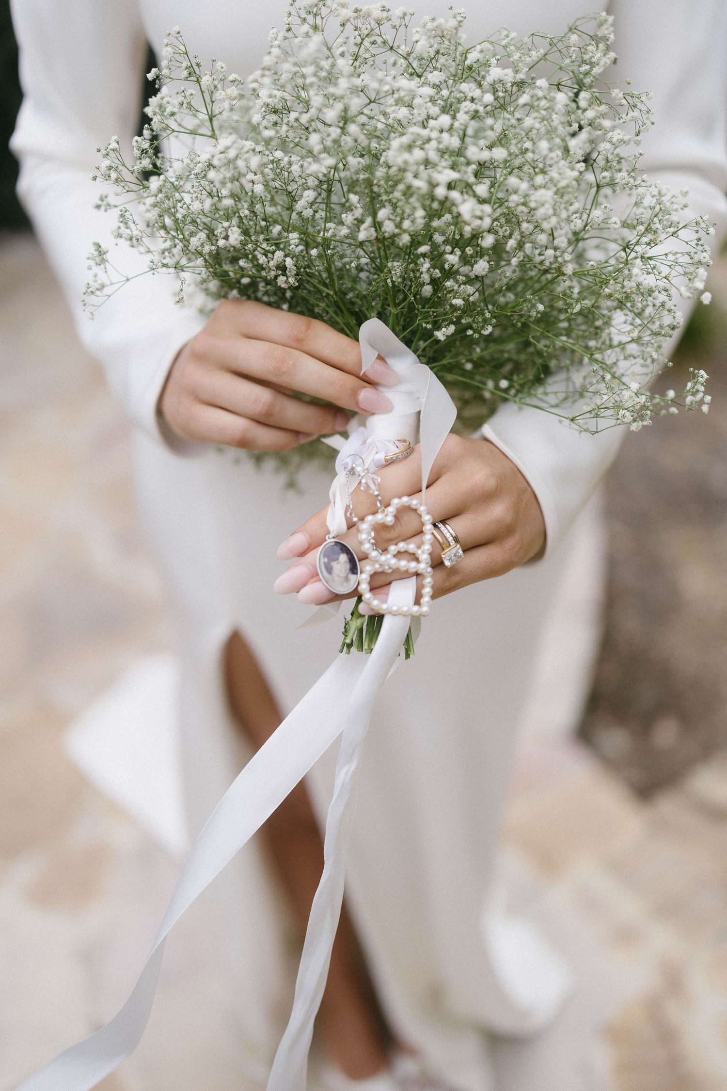 Bride holding a delicate white gypsophila wedding bouquet with pearl ribbon and white satin streamers.