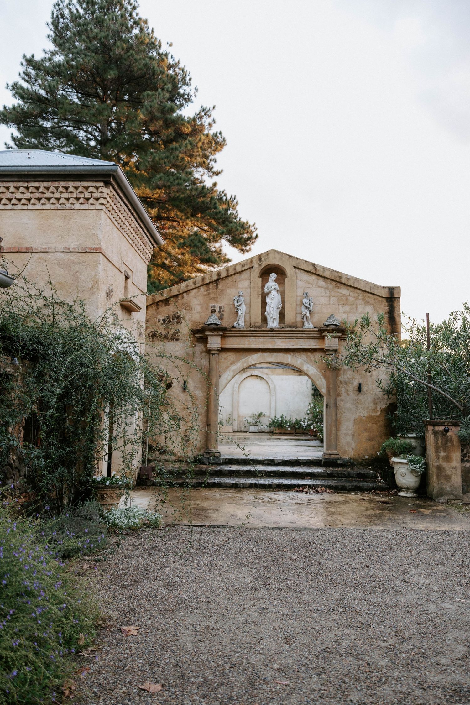 Ancient stone archway with classical statues, steps, and lush greenery in a historic garden courtyard.