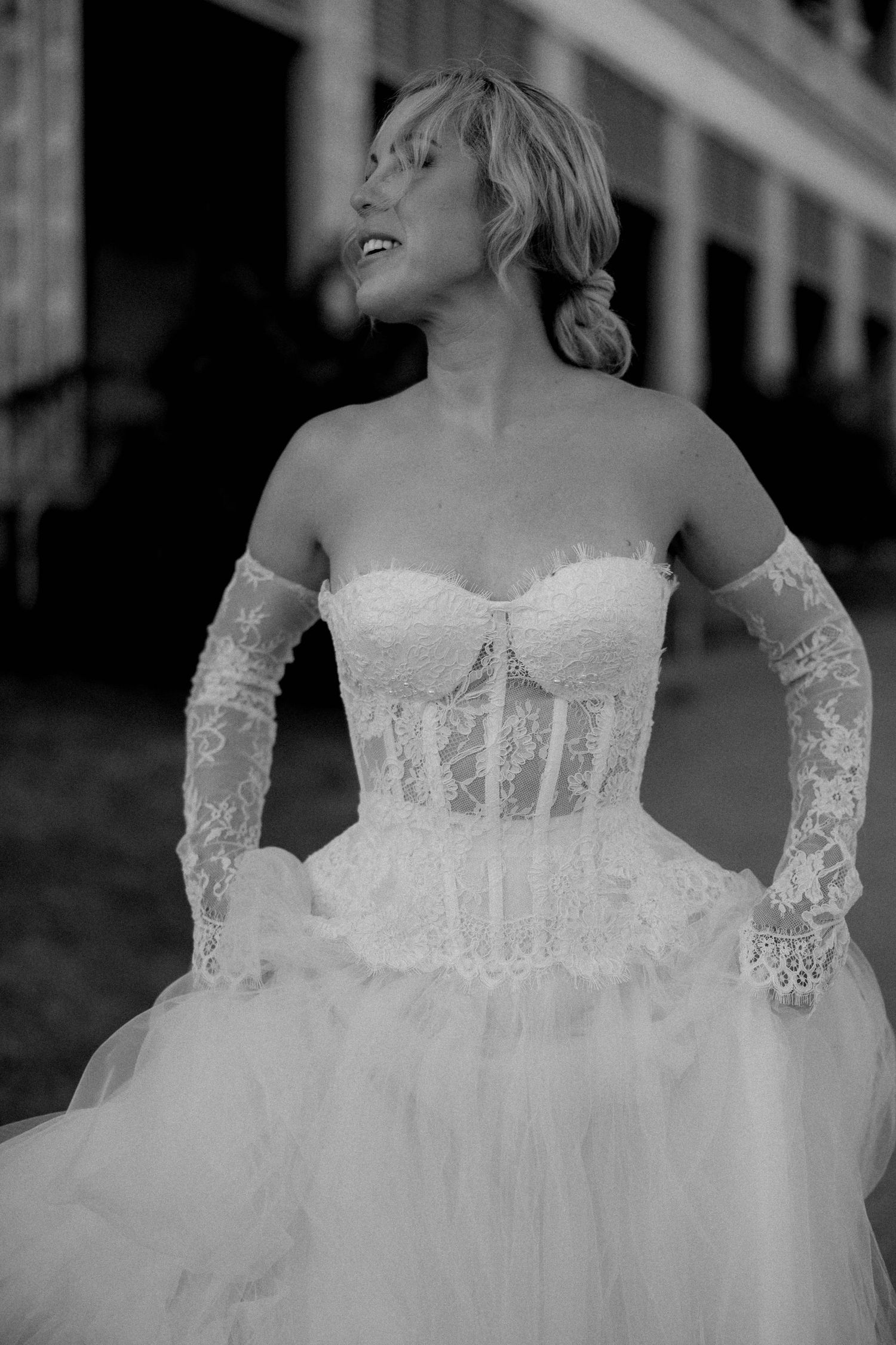 Black and white photo of a bride in a strapless lace corset wedding dress with delicate lace gloves and tulle skirt.