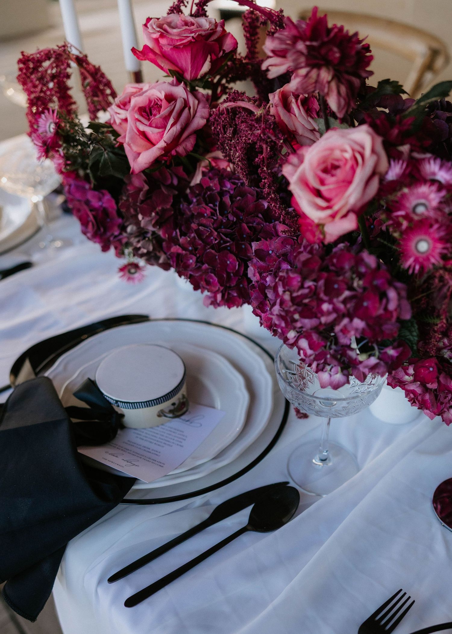 Elegant table setting with pink and burgundy floral arrangements alongside white plates and black napkins.