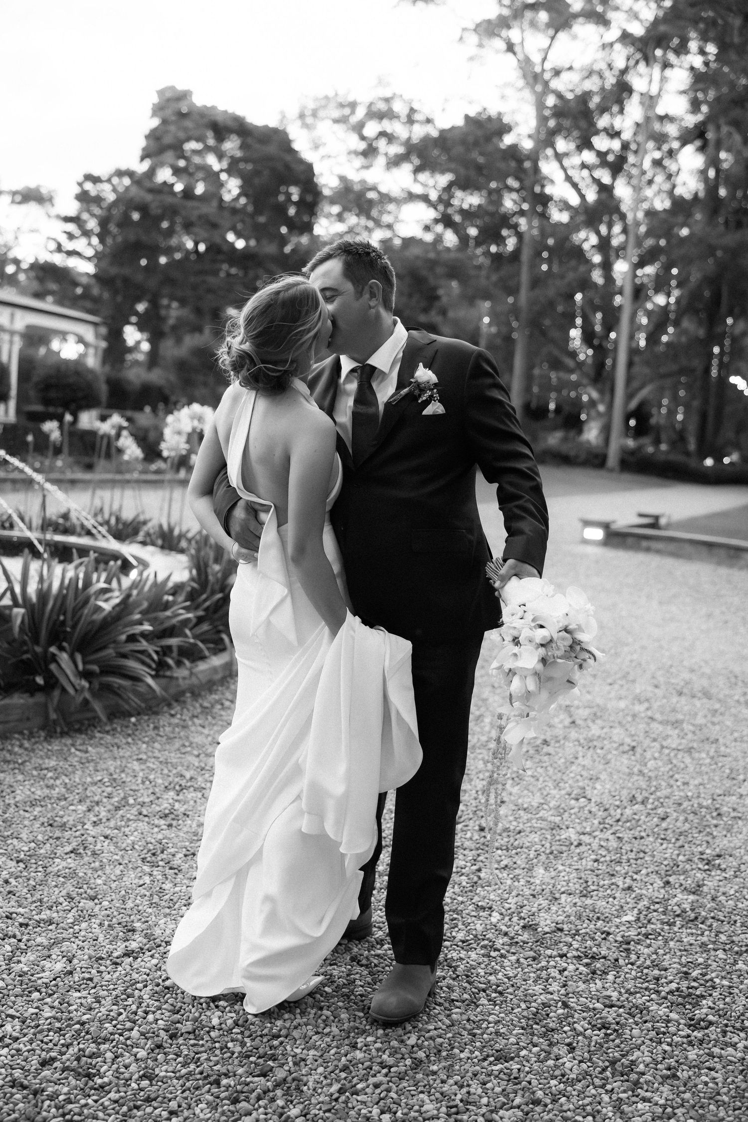 Black and white wedding photo showing a romantic moment between newlyweds embracing on a garden path.