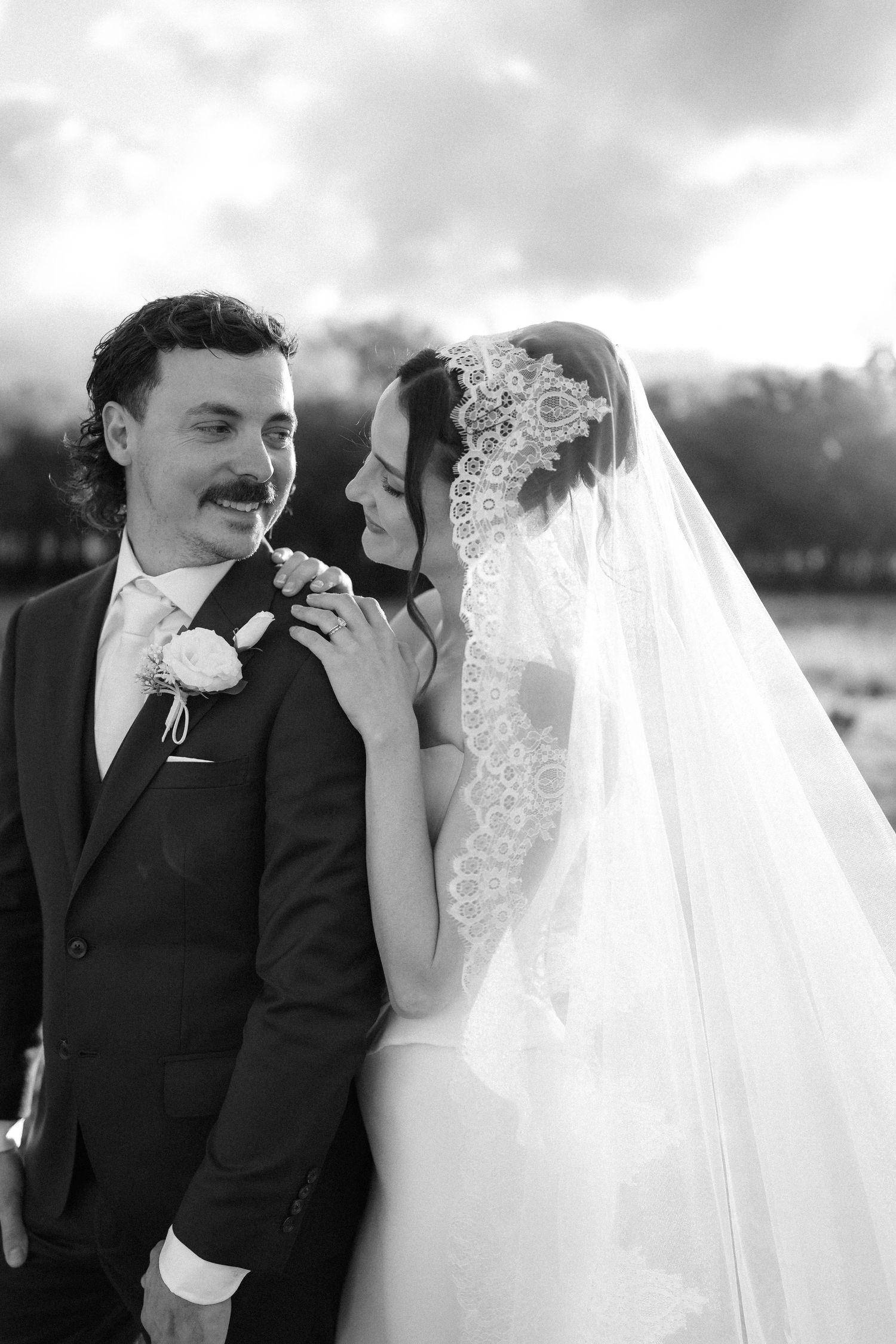 Black and white wedding photo of bride in lace veil embracing groom in dark suit with boutonniere outdoors. Warwick photographer