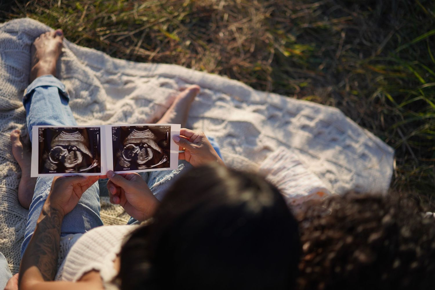 expecting couple looking at sonogram photo over couple's shoulder on a picnic blanket
