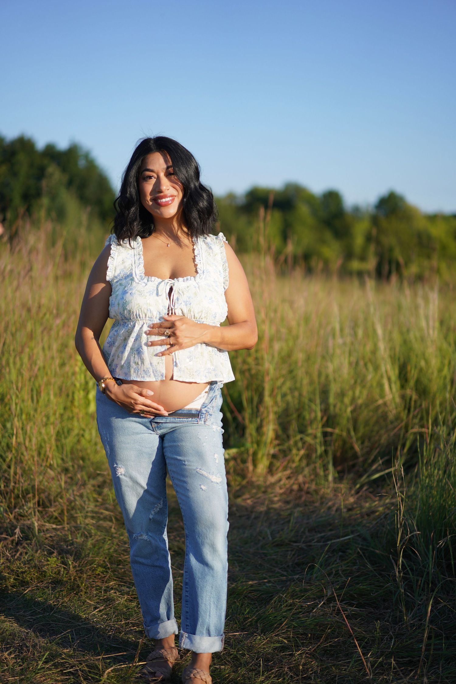 mom to be holding belly in field, blue skies