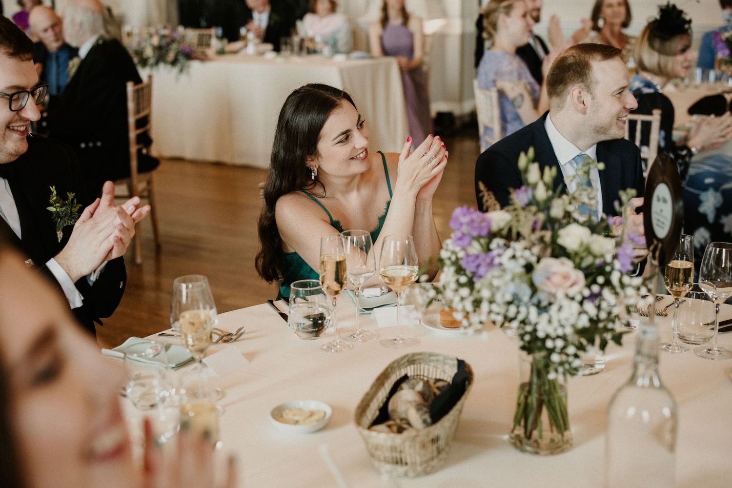 Wedding reception guests enjoying dinner at elegantly decorated tables with floral centerpieces.