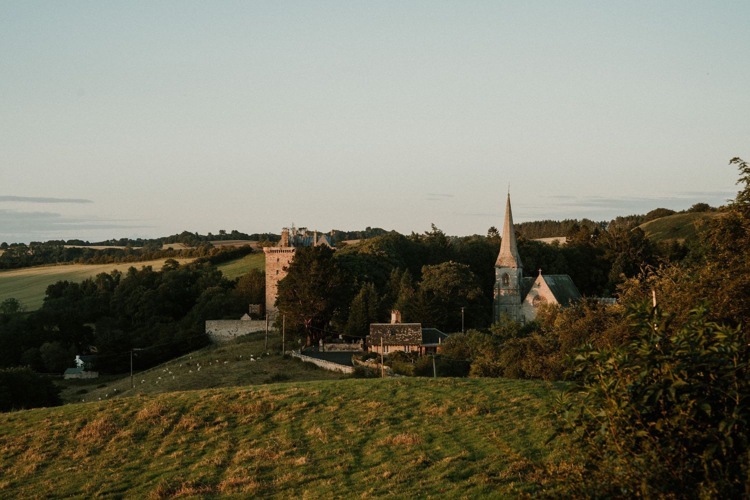 A panoramic view of rolling countryside hills with church spires and buildings dotting the rural landscape at sunset.