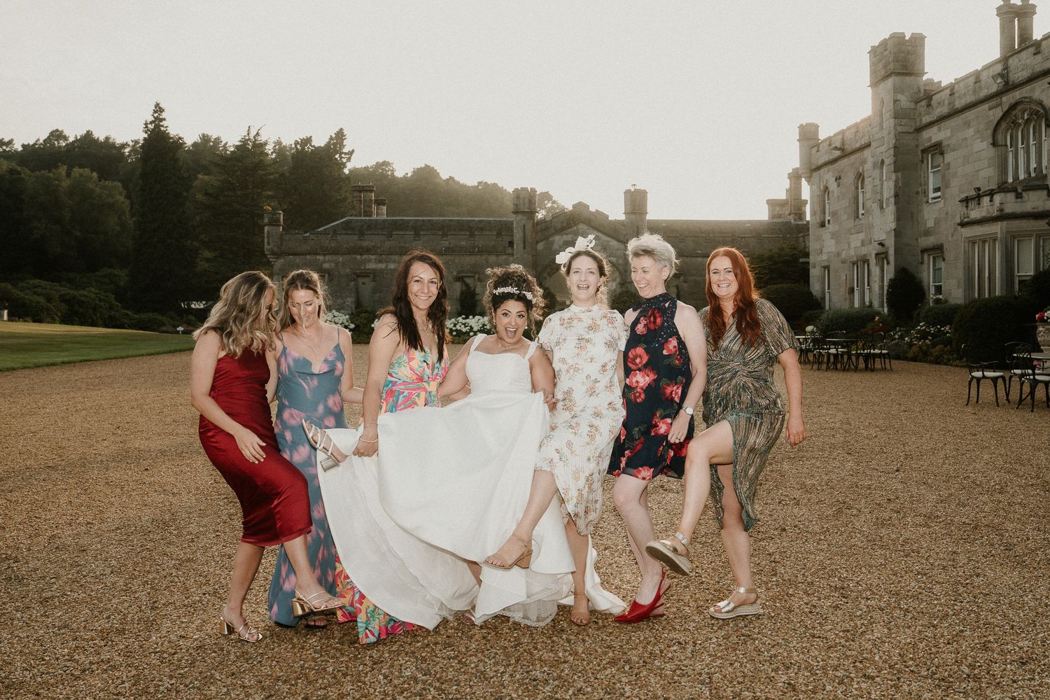 A wedding party in colorful attire poses together on the grounds of a historic castle.