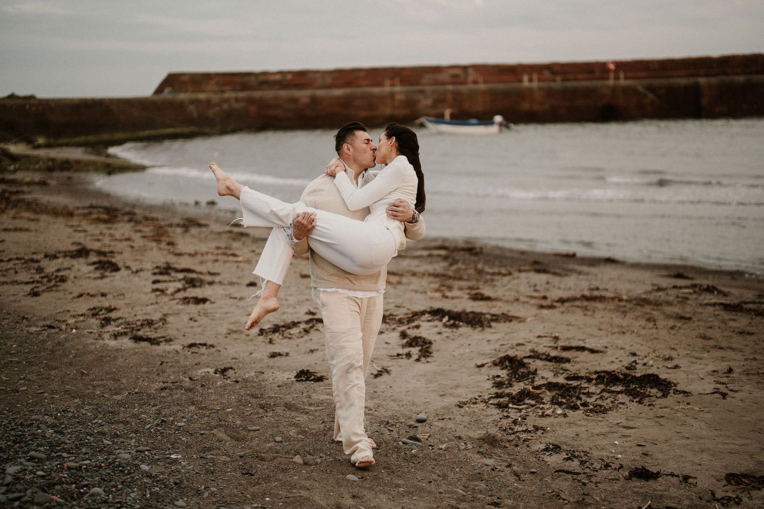 Playful couple moment on a beach with dramatic cliffs in the background.