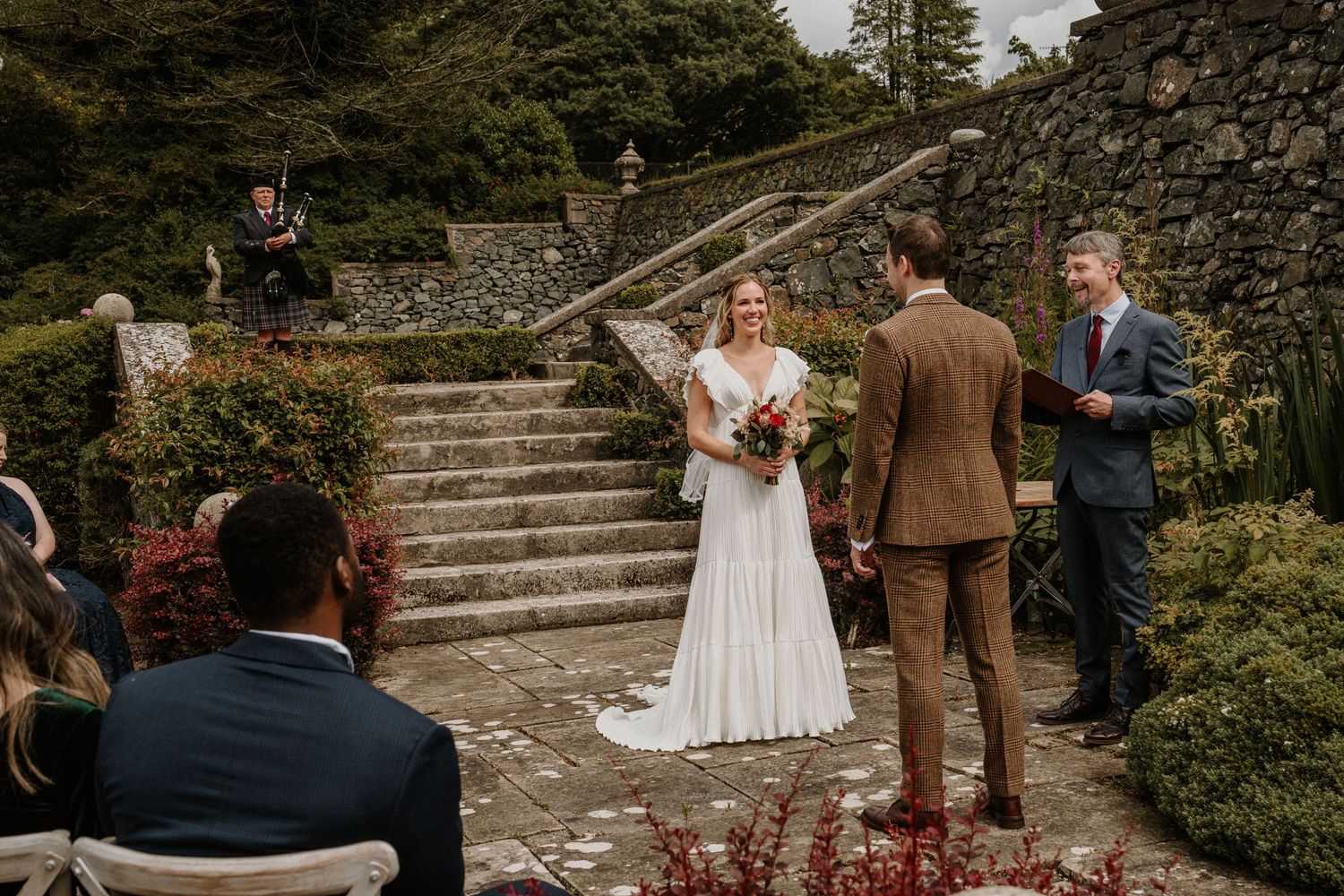 Outdoor wedding ceremony on stone steps surrounded by lush gardens.