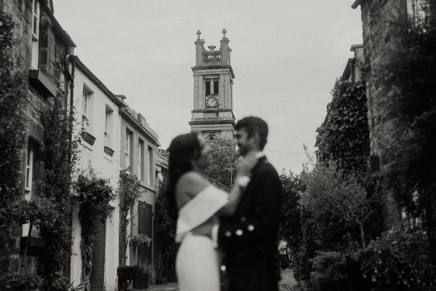Newlyweds share intimate moment on quaint cobblestone street in Scottish town.