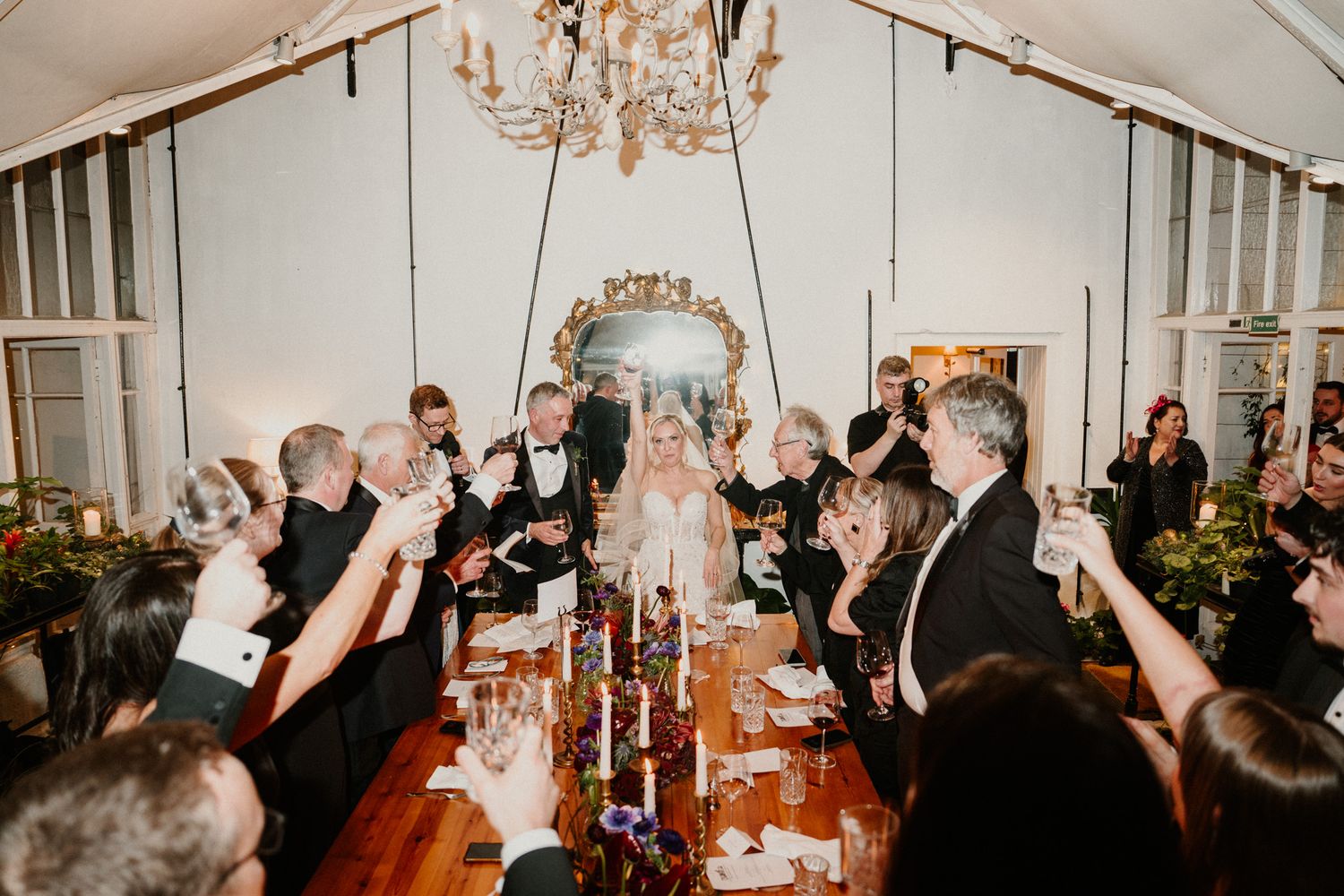 Wedding reception venue with vaulted ceilings, chandeliers, and guests celebrating at decorated tables.