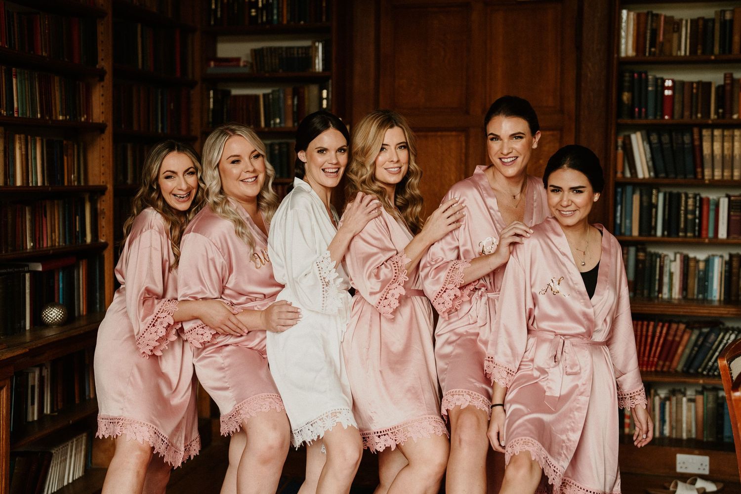 Wedding party in matching pink robes posing in a wood-paneled library.