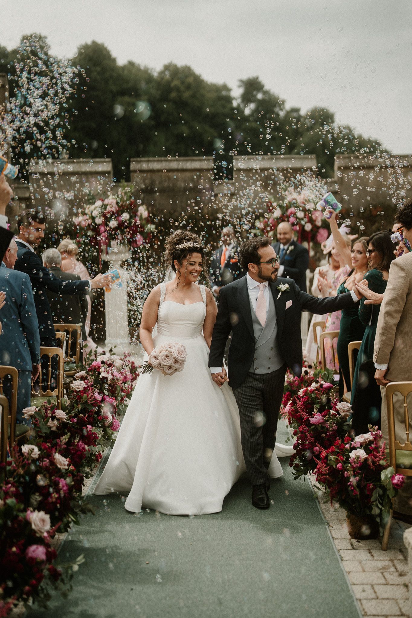 Wedding celebration with confetti toss and pink floral arrangements lining the aisle.