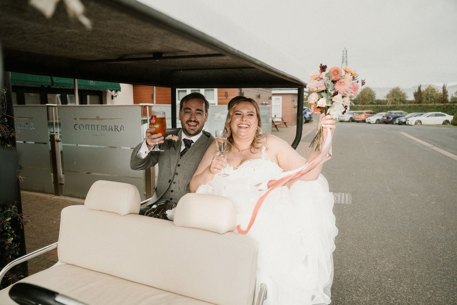 A wedding party poses in front of a white limousine on a cloudy day.