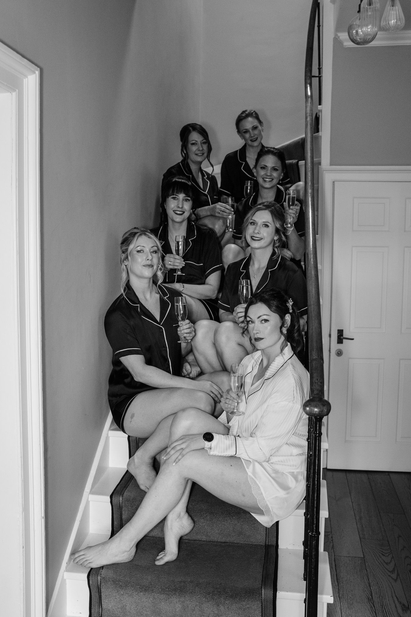 A group in white robes relaxes and laughs together in a casual pre-wedding preparation setting.