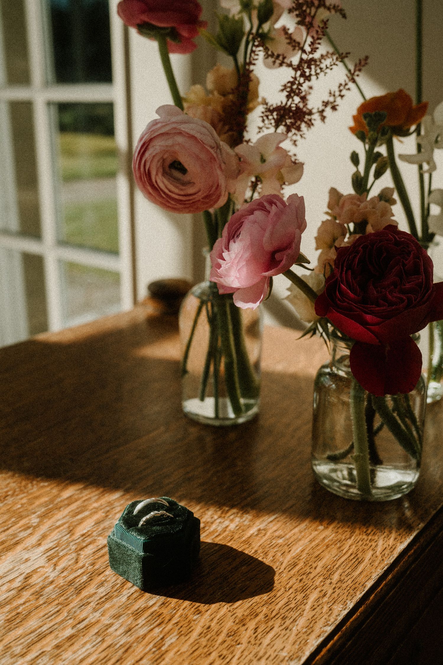 Romantic flower arrangements with pink and red roses in glass vases on wooden table.