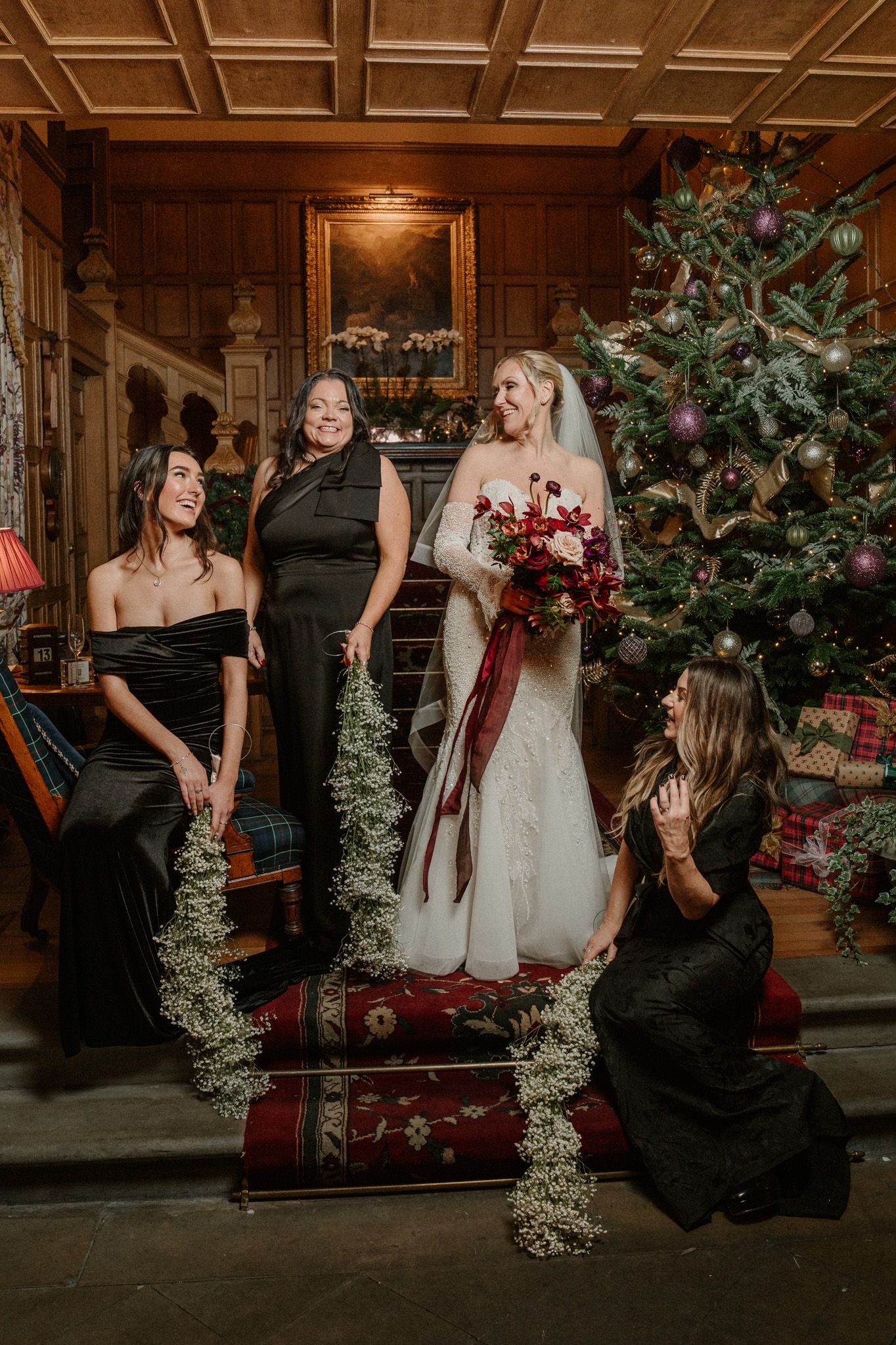 Wedding party gathered on ornate staircase with Christmas decorations and wood-paneled walls.