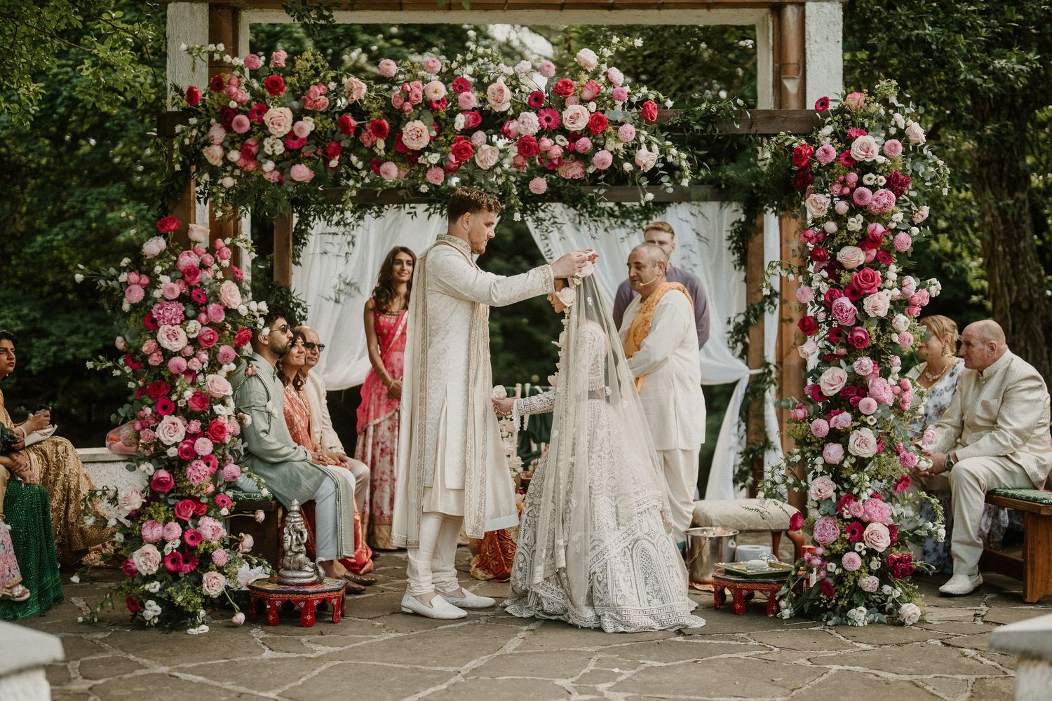 Outdoor wedding ceremony space decorated with abundant pink and red roses on an elegant wooden arch.