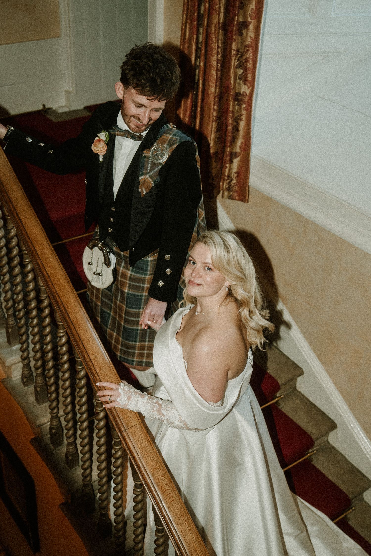 A couple shares a romantic moment on an elegant staircase with ornate railings at their wedding celebration.