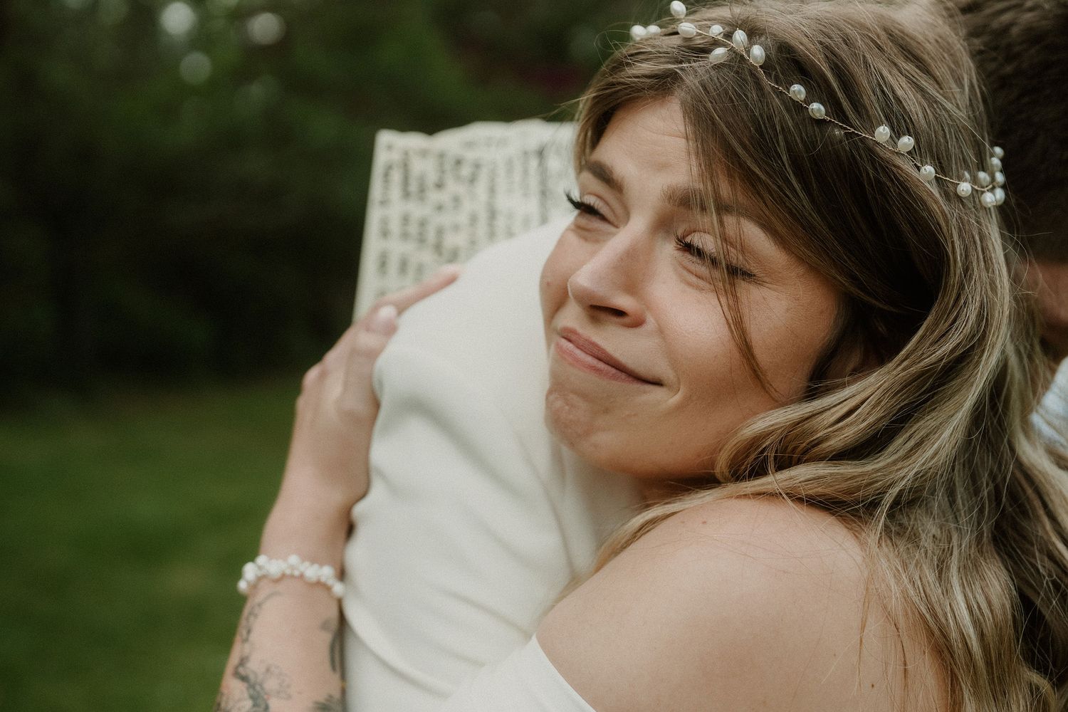 Emotional bride with floral hair crown shares a heartfelt hug during wedding day celebration outdoors.