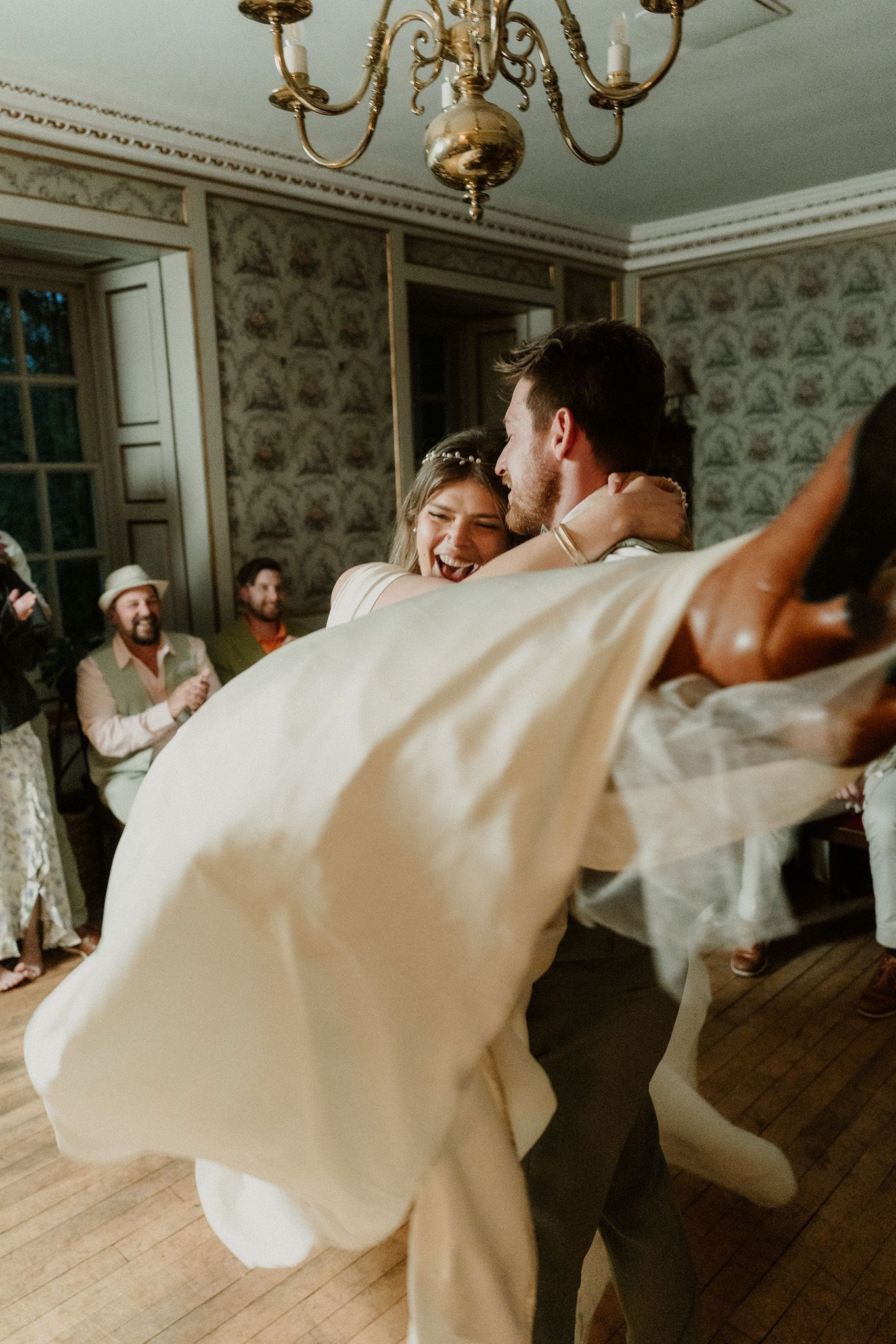 Groom joyfully lifts laughing bride in wedding dress during first dance at elegant reception.