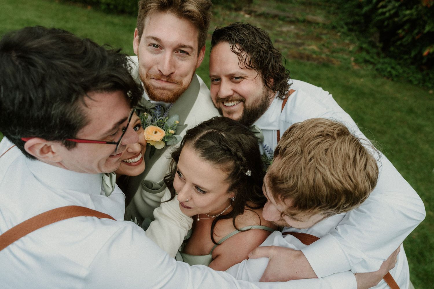 Group of groomsmen in white shirts hugging a young girl outdoors at a wedding celebration.