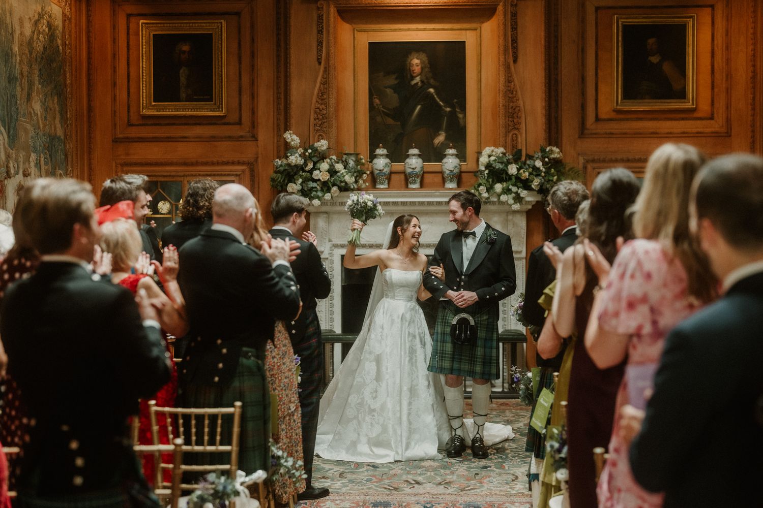 Bride and groom celebrate at wedding ceremony in elegant wood-paneled room with guests applauding.