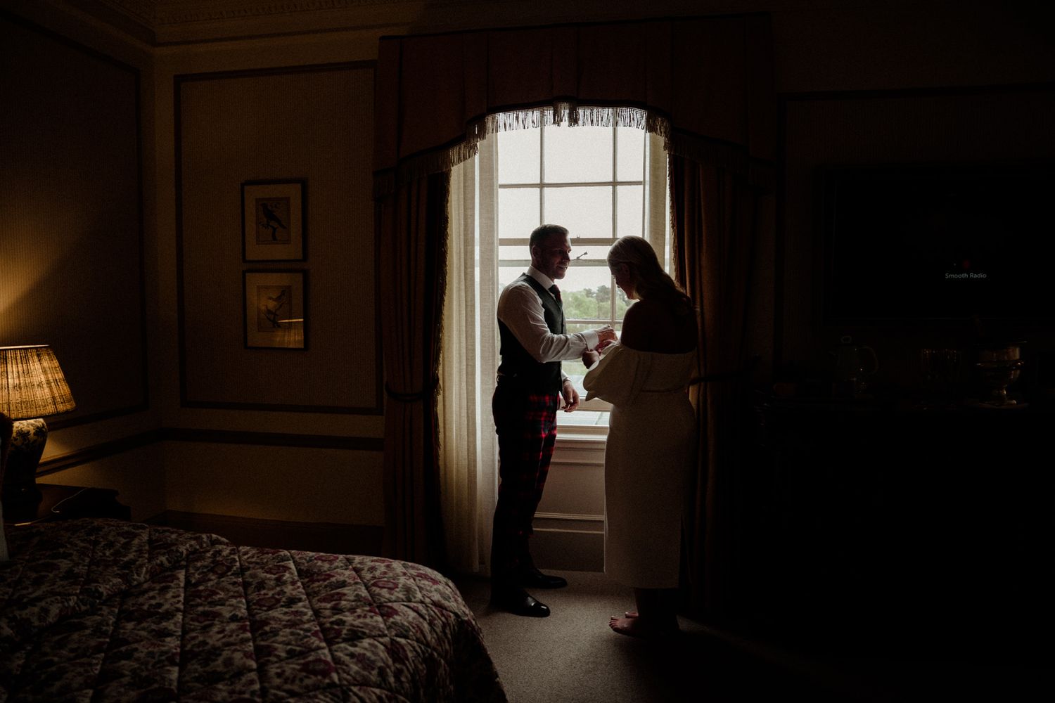 Silhouetted figures stand in dramatic window lighting during wedding preparations.